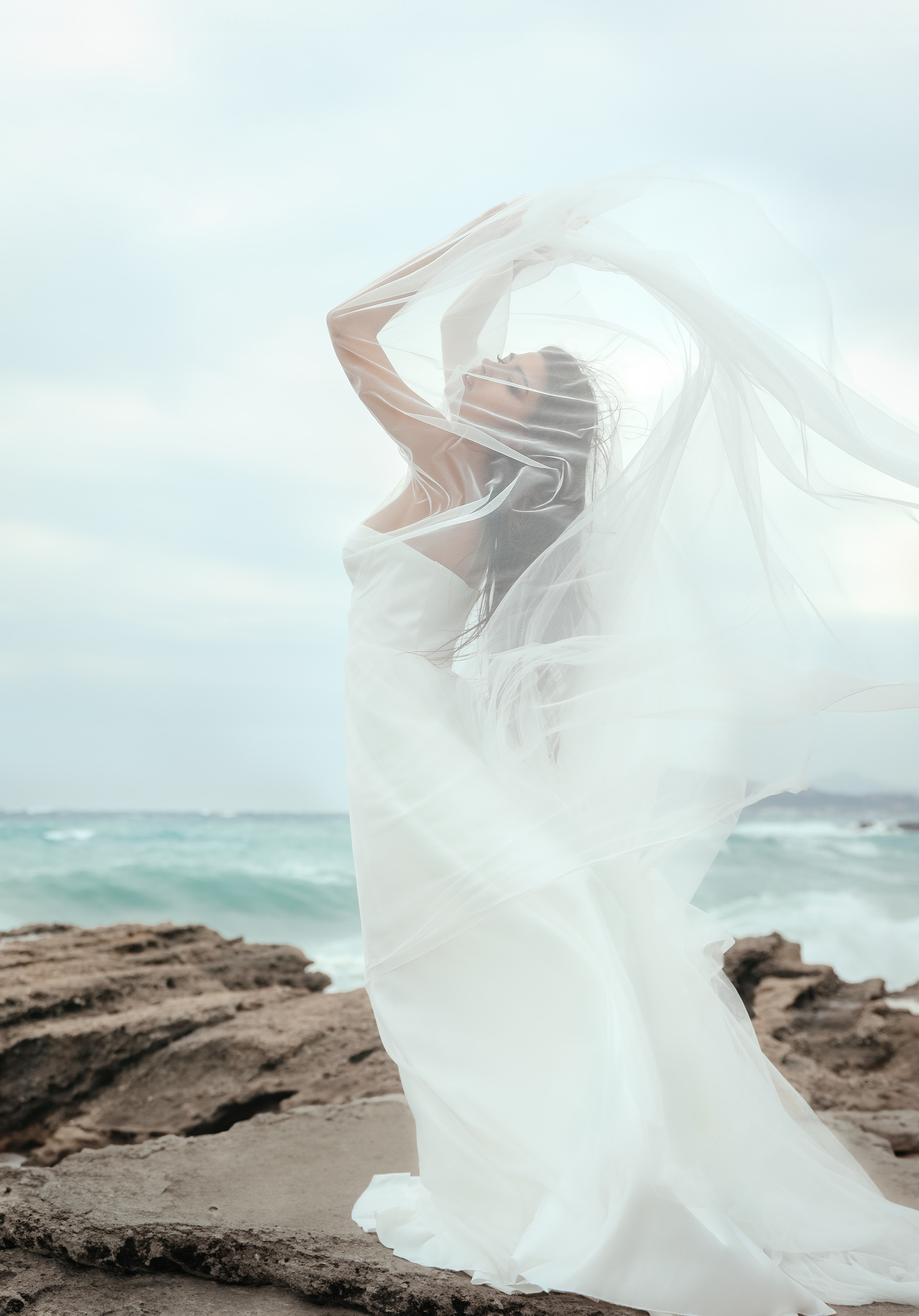 An art photo shoot of a girl in a wedding dress on the windy Kalithea beach in Rhodes, Greece