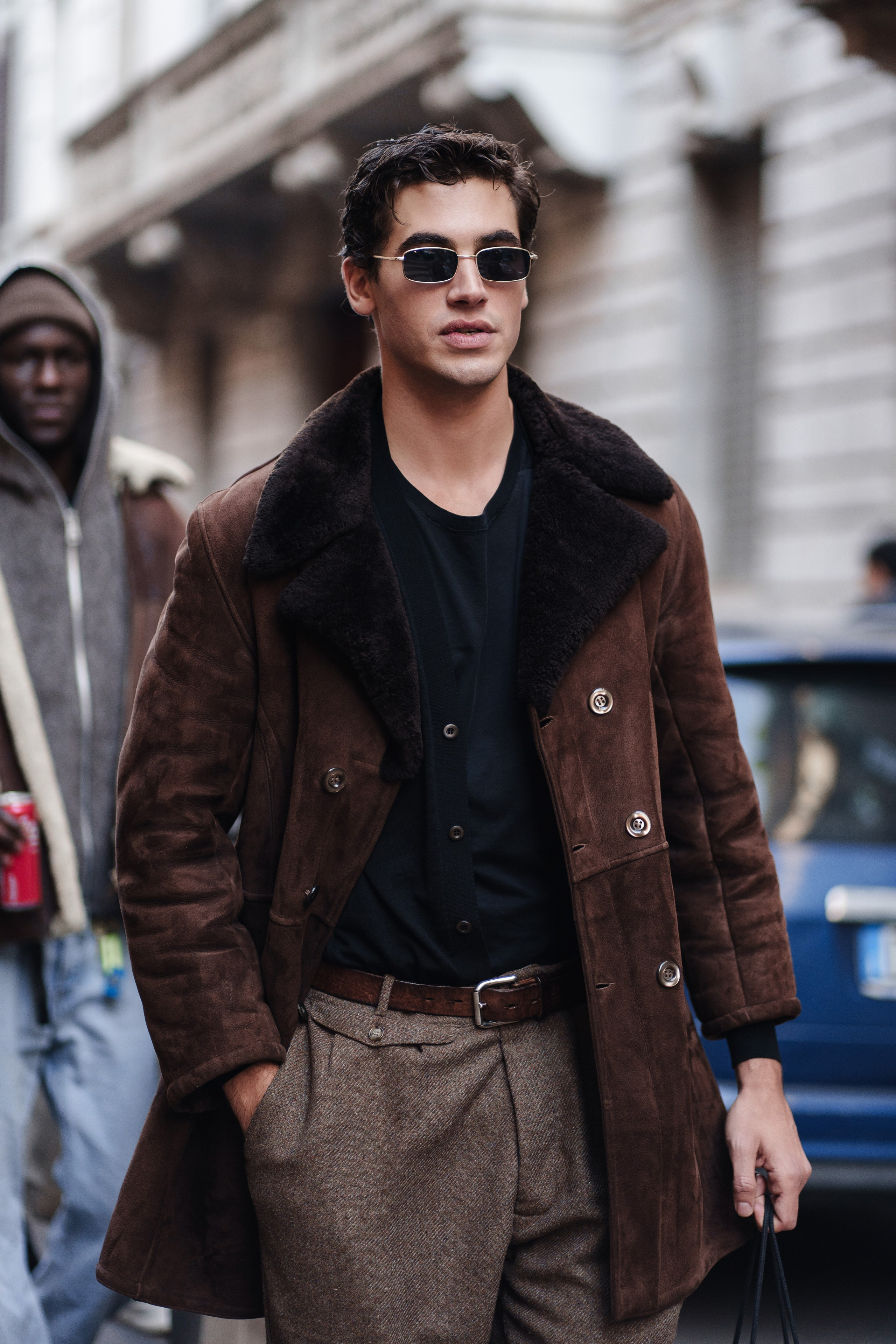 Trendy young man in sunglasses and a brown shearling coat at Milan Fashion Week