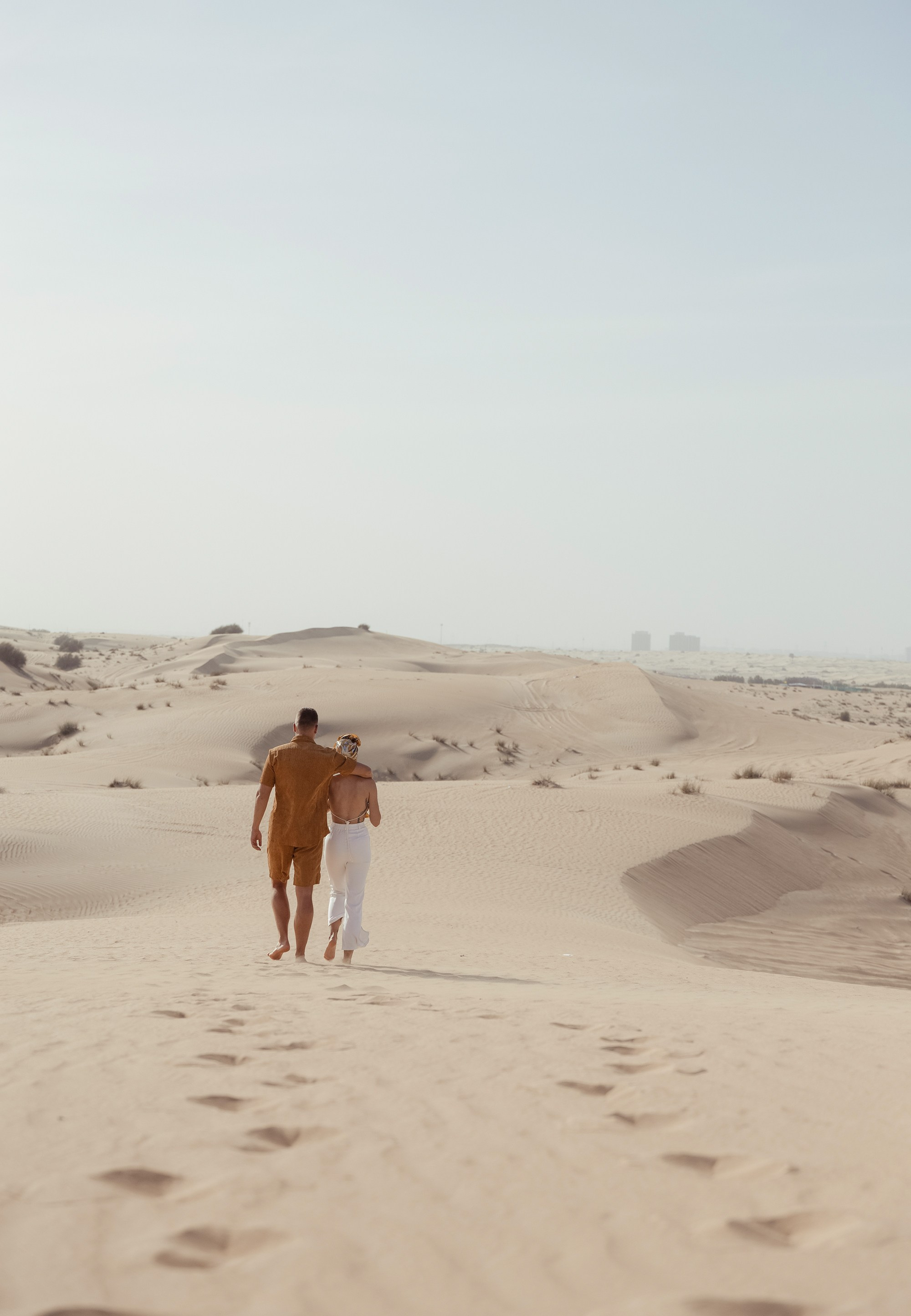 A romantic desert scene: a couple hugs, their silhouettes glowing under the warm sunset light. Dubai, United Arab Emirates