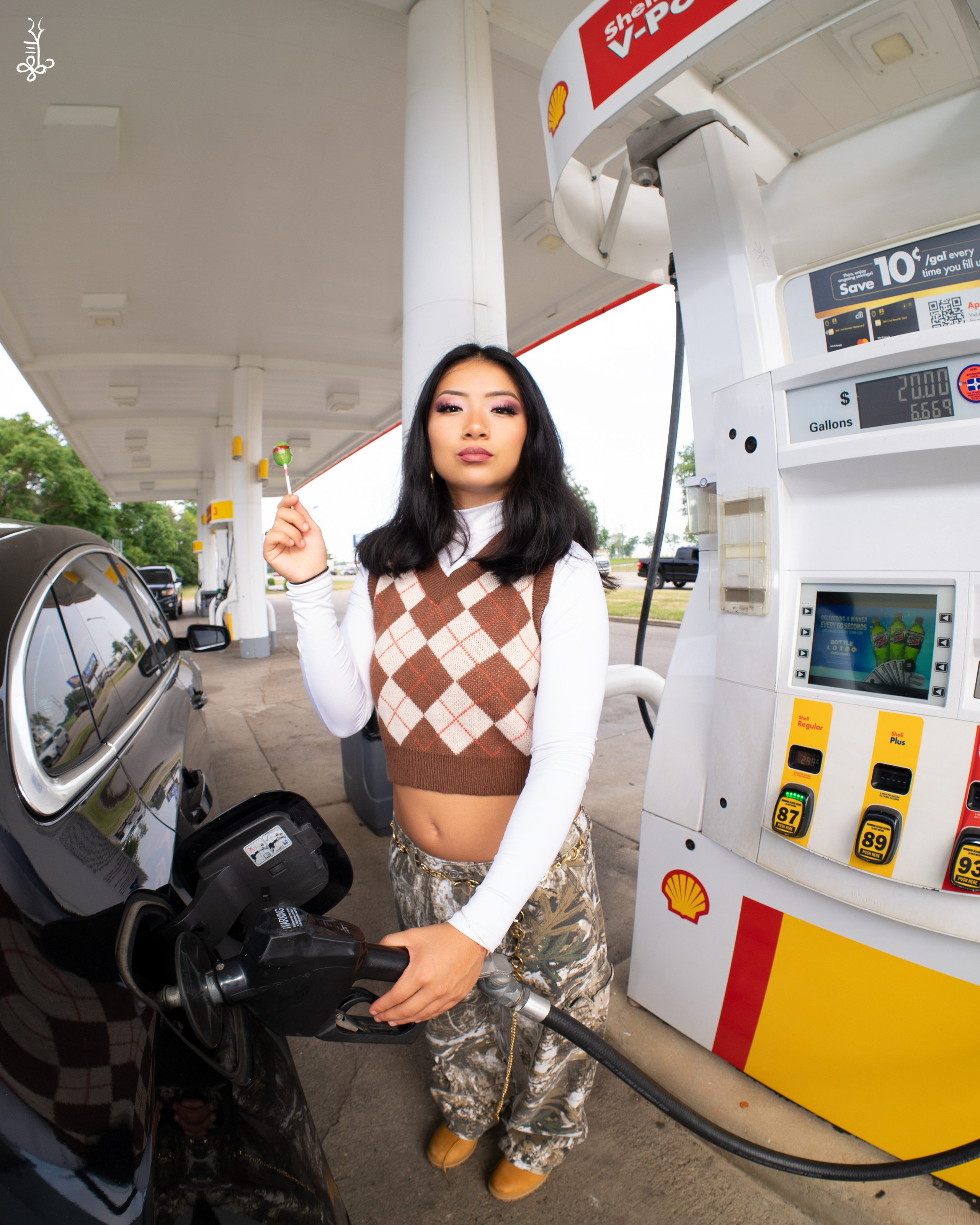 Model leaning against gas pump wearing brown checkered vest and khaki pants