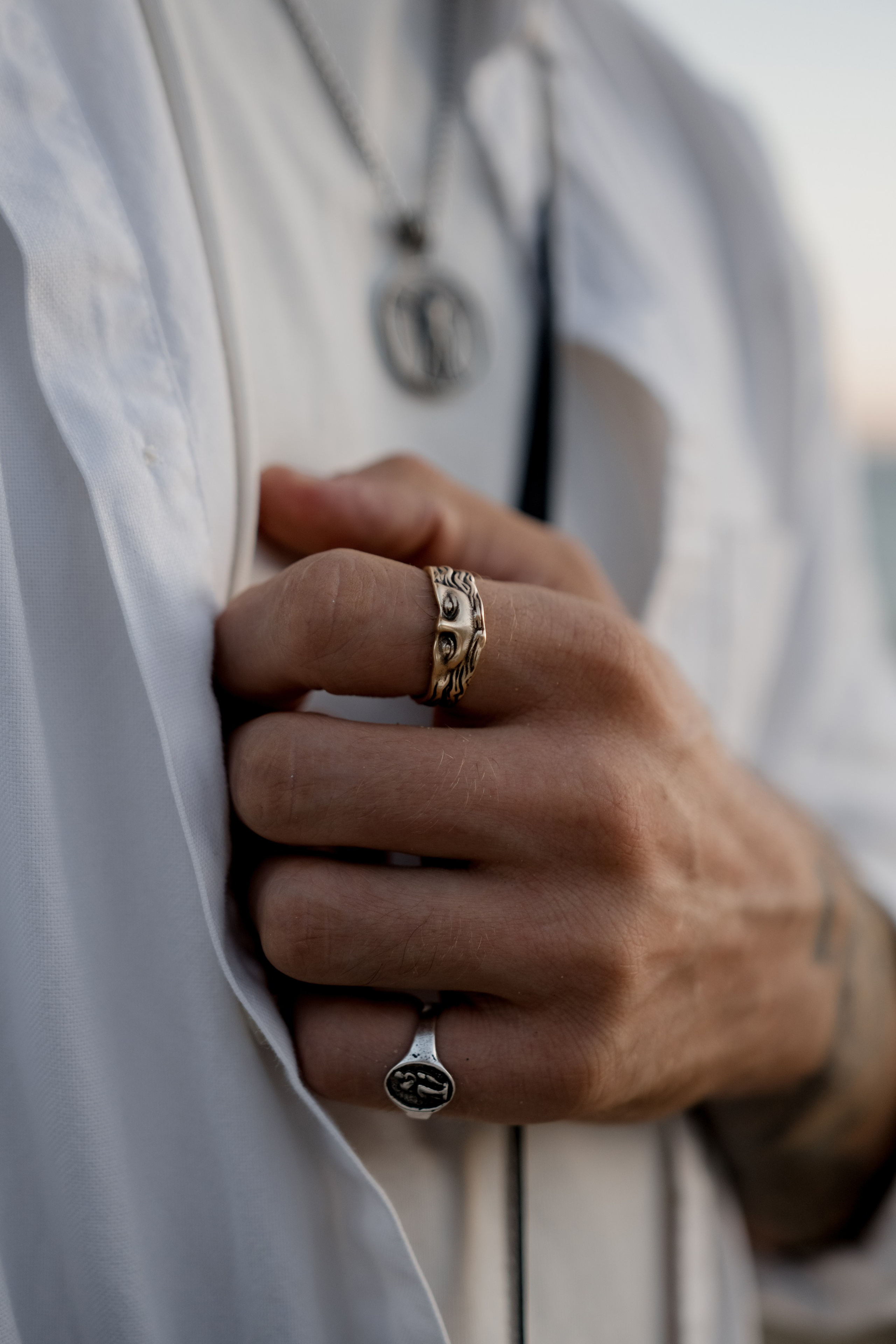 Detailed shot of a pendant necklace with artistic engravings styled on a white shirt, blending elegance and casual wear.