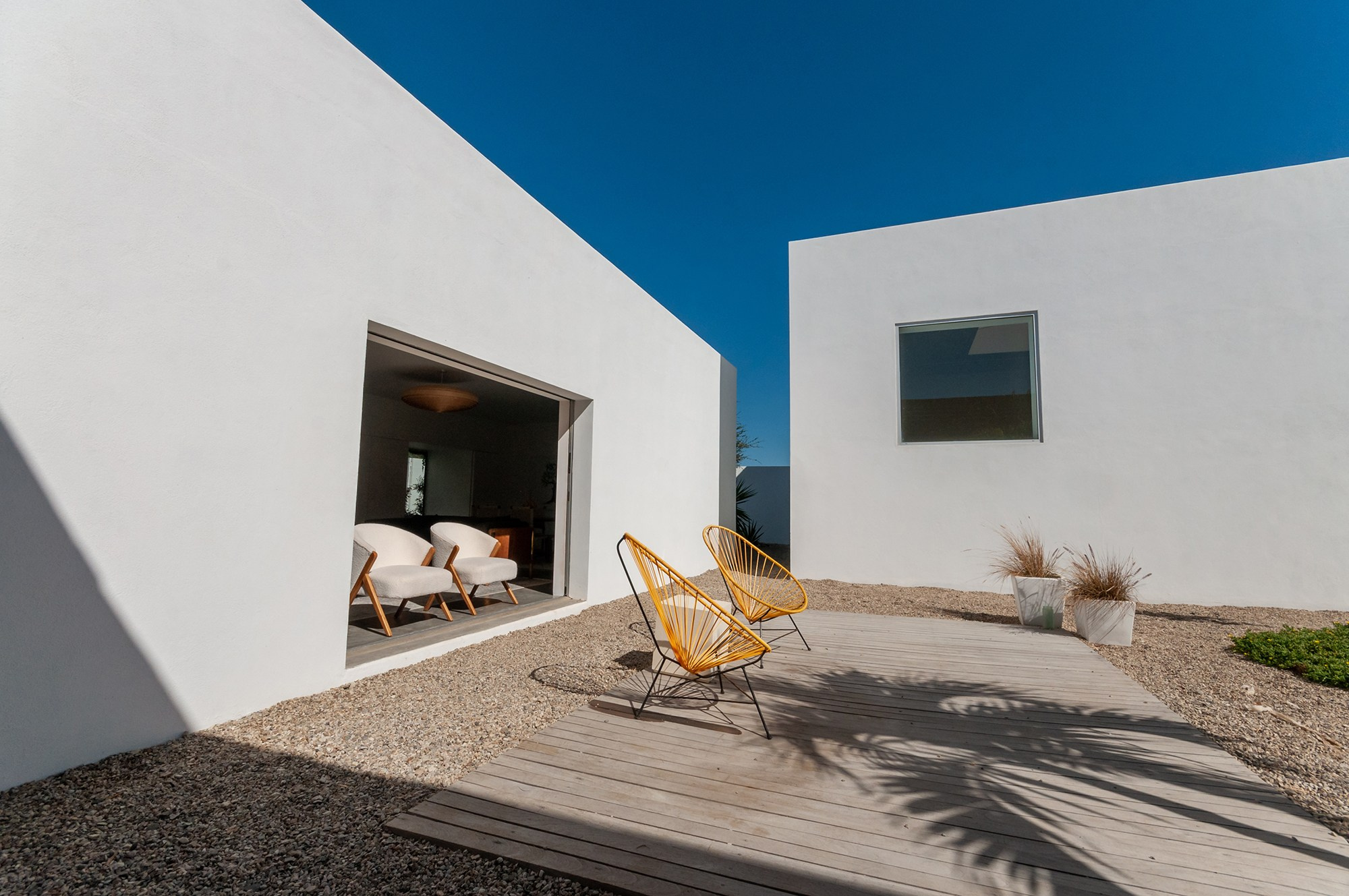 Minimalist white exterior home in Todos Santos – clean volumes, garden lounge area and palm shadows, luxury real estate photography