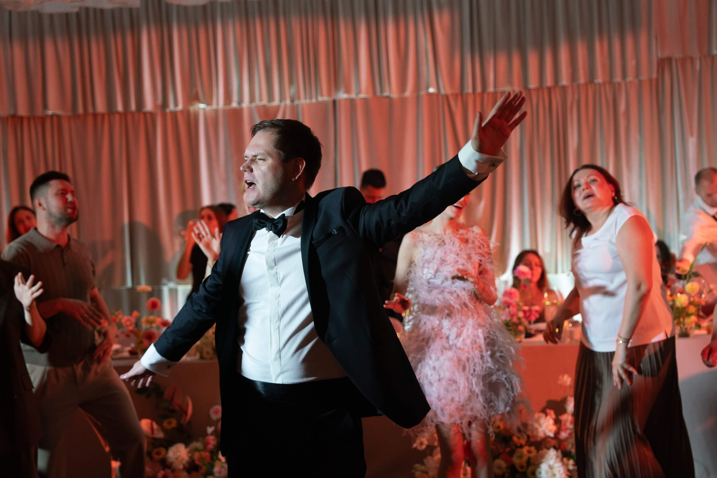 Groom energetically dancing with arms raised under warm orange stage lighting at the wedding reception party, Lake Como wedding ceremony