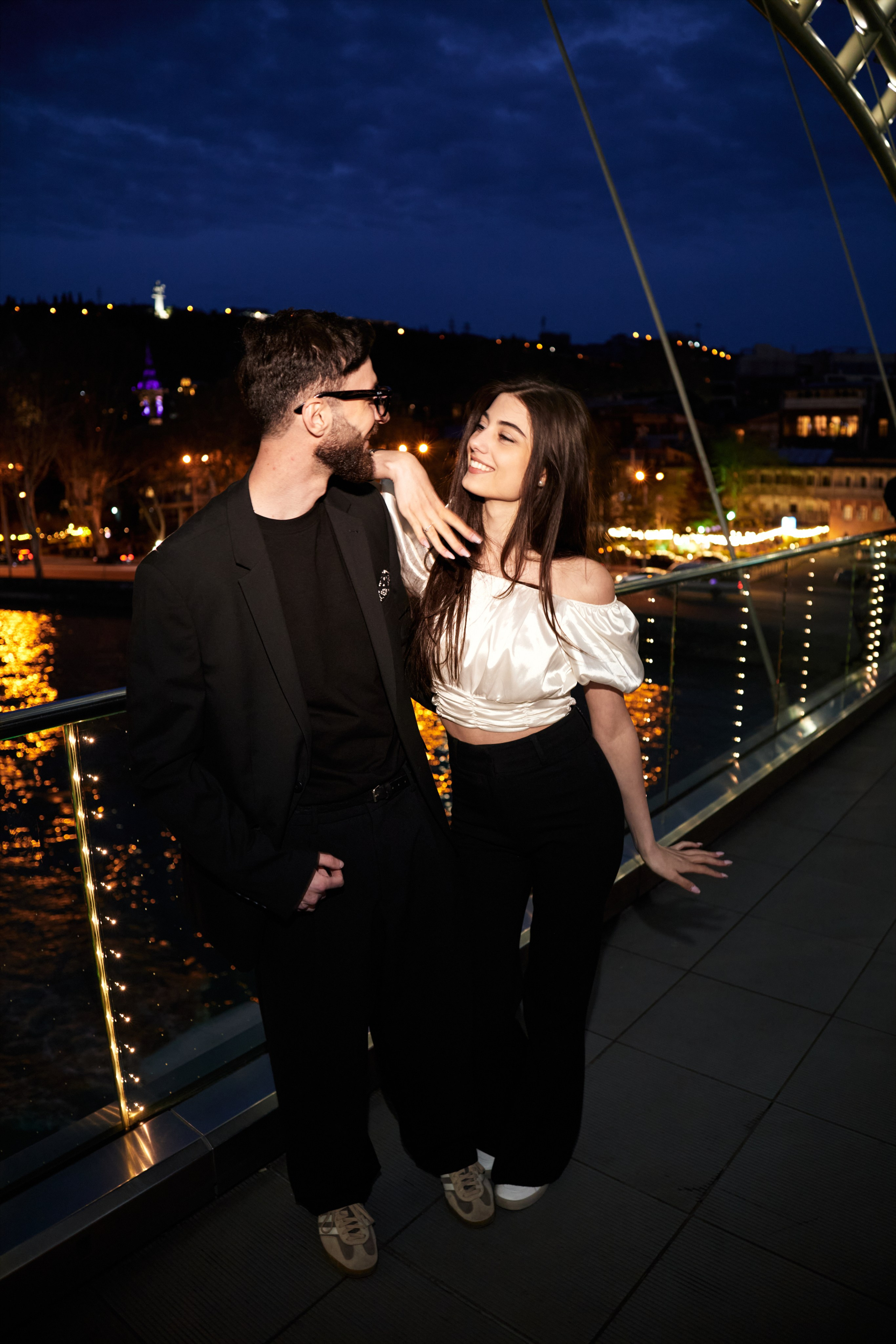 Парень и девушка сидят на пирсе у реки, нежные объятия во время Love Story съёмки.