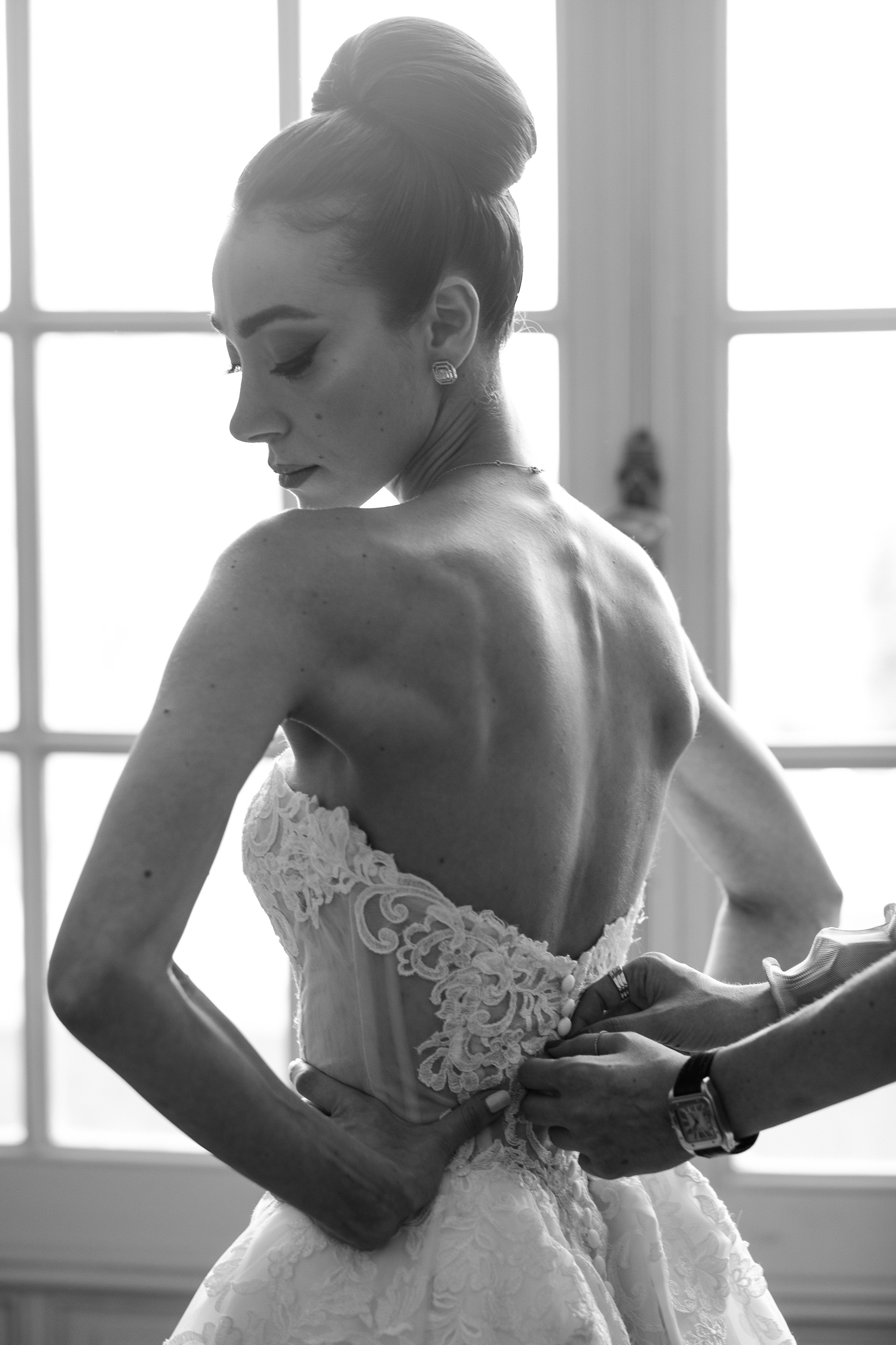 Elegant bridal preparation in France with a close-up detail of the wedding dress being fastened, captured in black and white