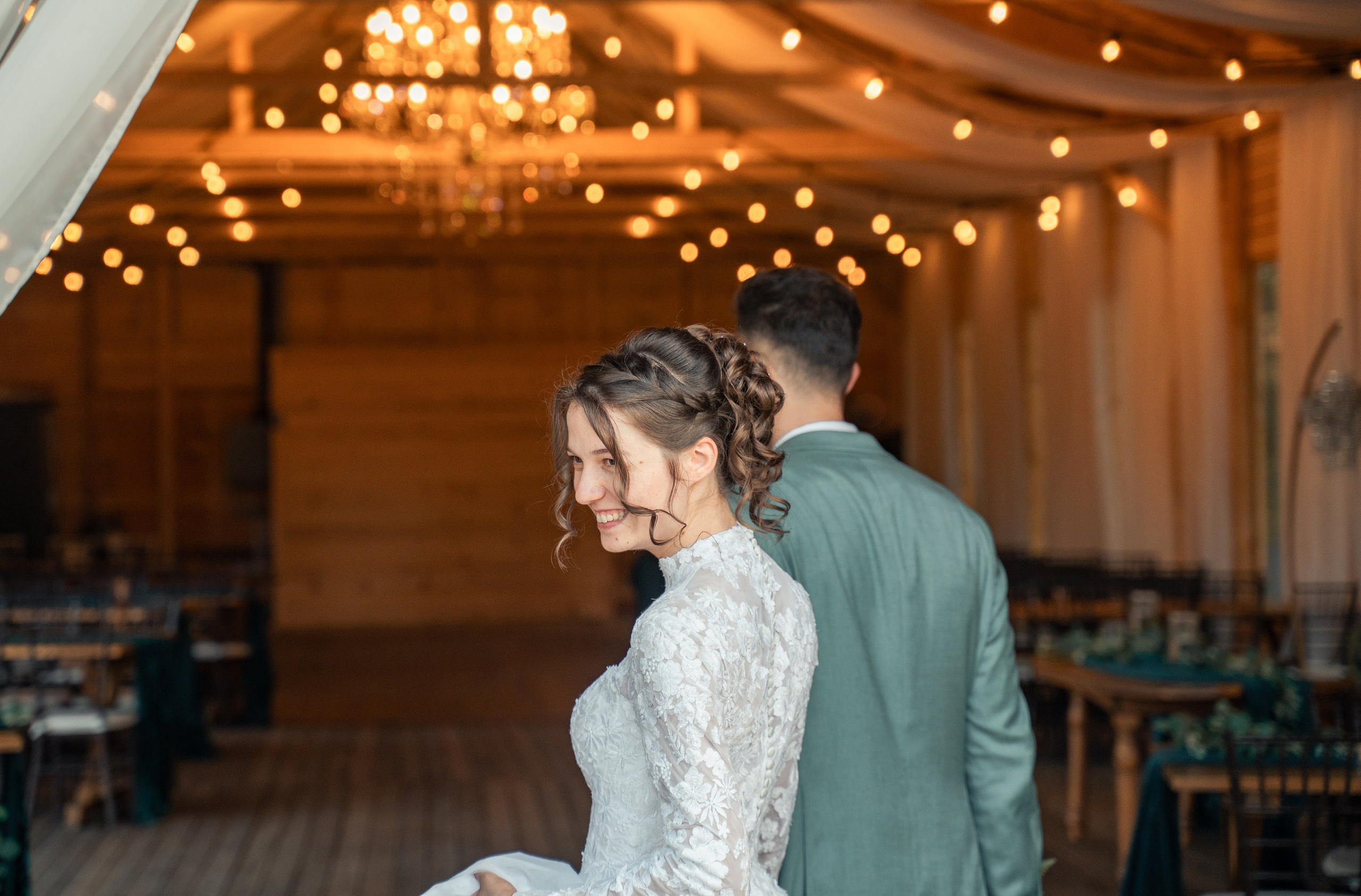 Vedere din spate cu mirii intrând în sala de recepție decorată cu candelabre și luminițe, rochie de mireasă cu nasturi, incadru.ro.