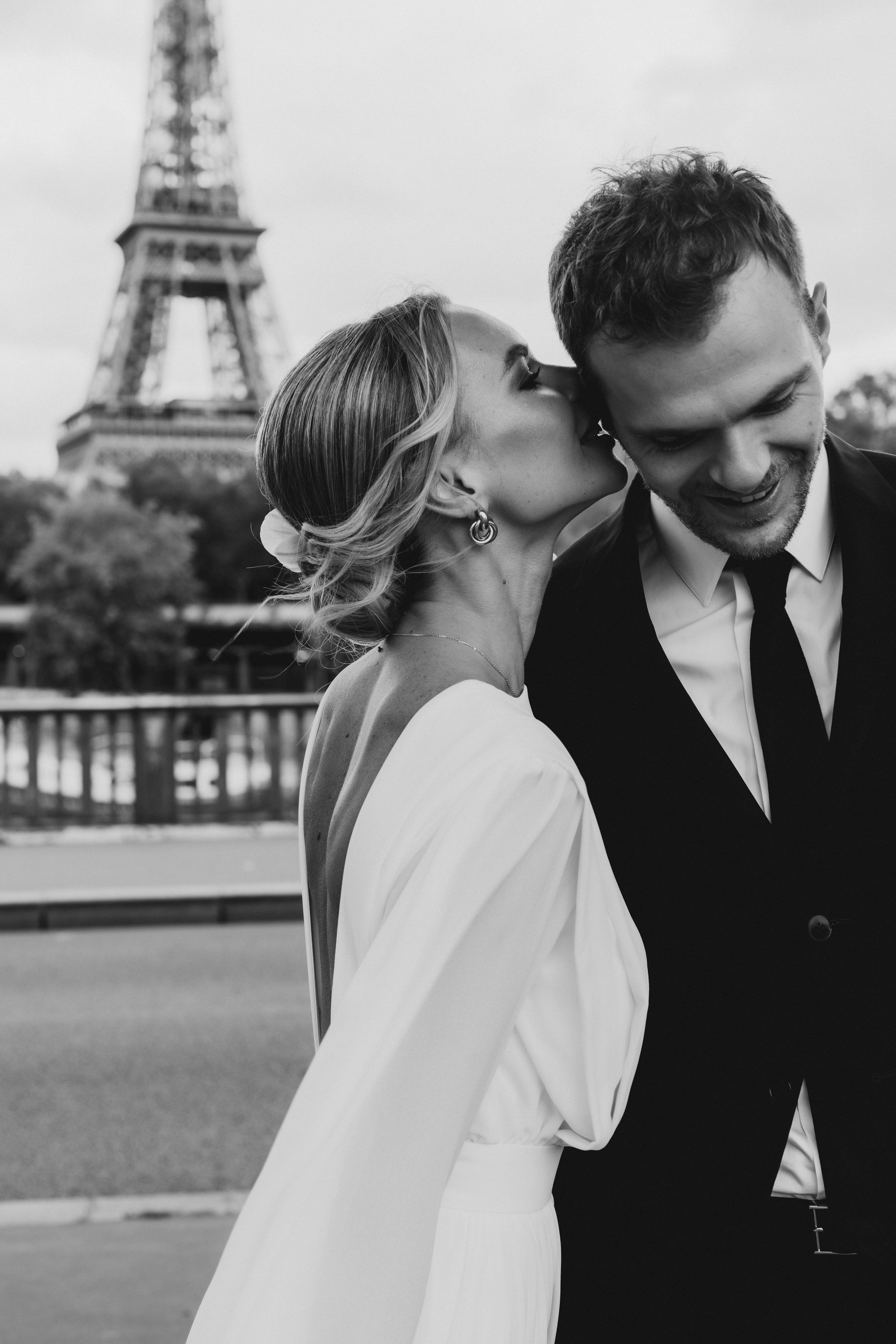 Bride kissing groom near the Eiffel Tower in Paris, intimate luxury Paris wedding photography in black and white
