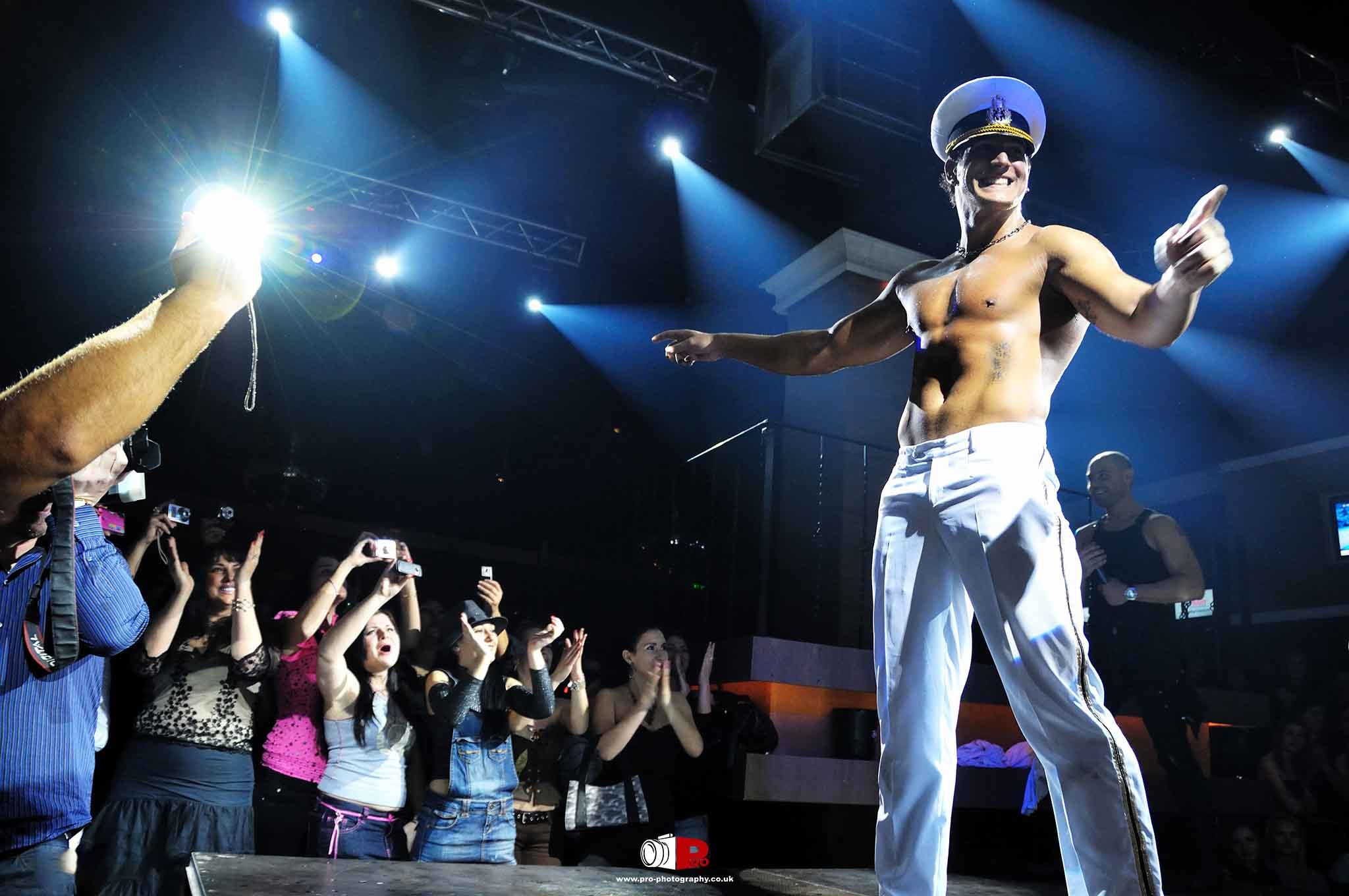 Stage performer dressed as a sailor, entertaining a cheering crowd with energetic gestures during a nightclub show.