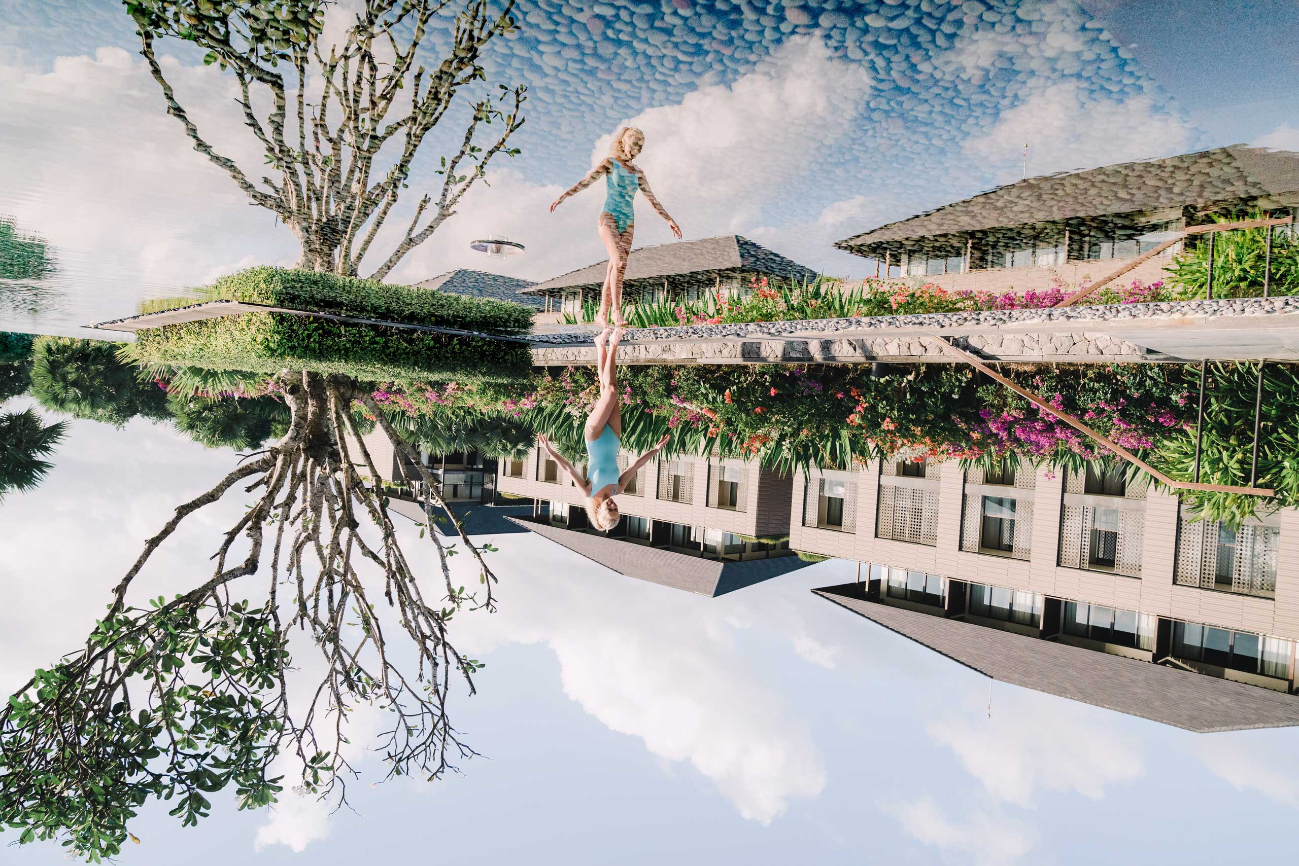 Beautiful young lady strolling near a swimming pool in a picturesque area with blue sky and flowers