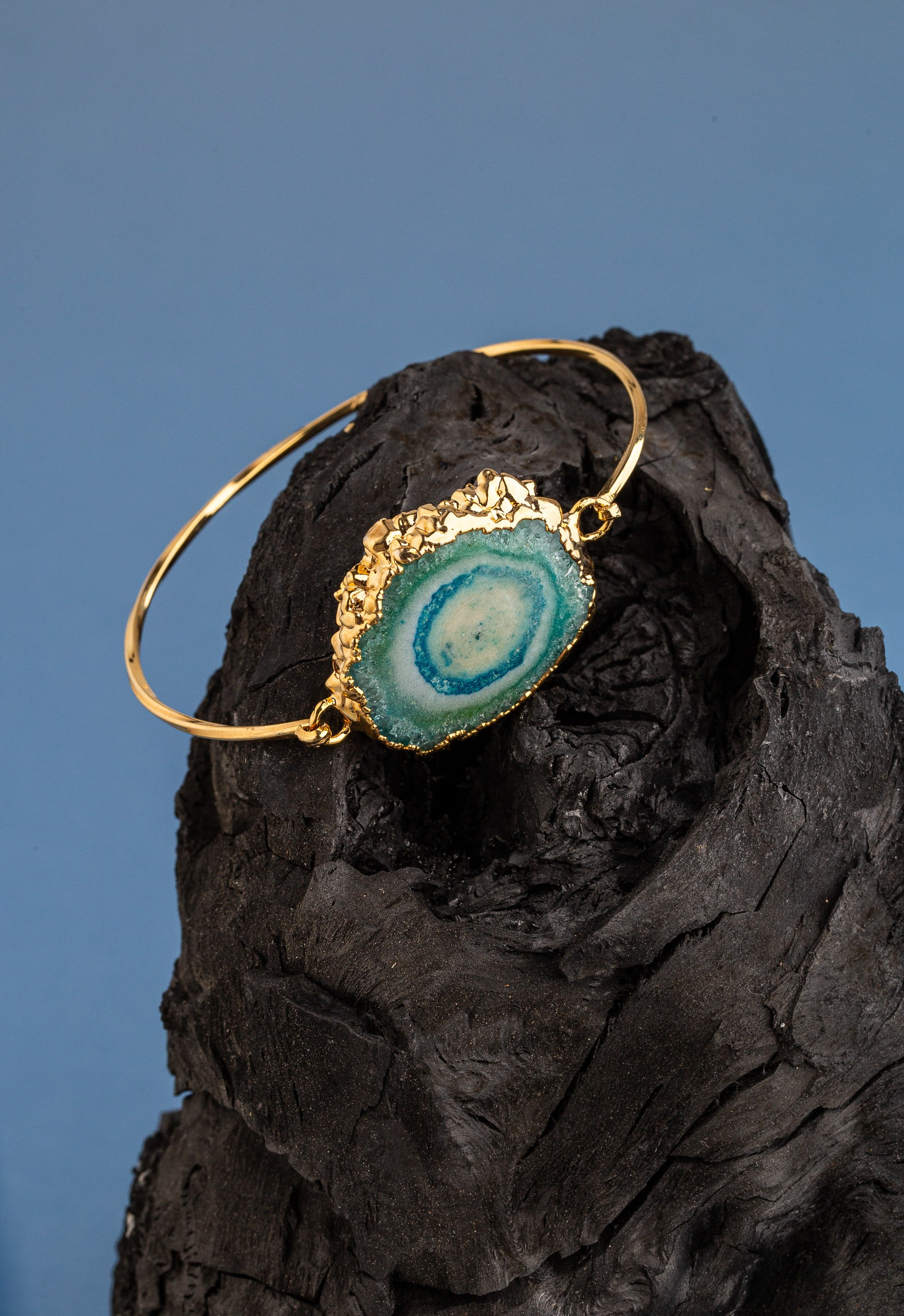 Tünd, teksturalı kömür və mavi fonda nümayiş etdirilən, orta hissədə mavi və ağ əqiq dilimli qızıl bilərzik bilərzik.