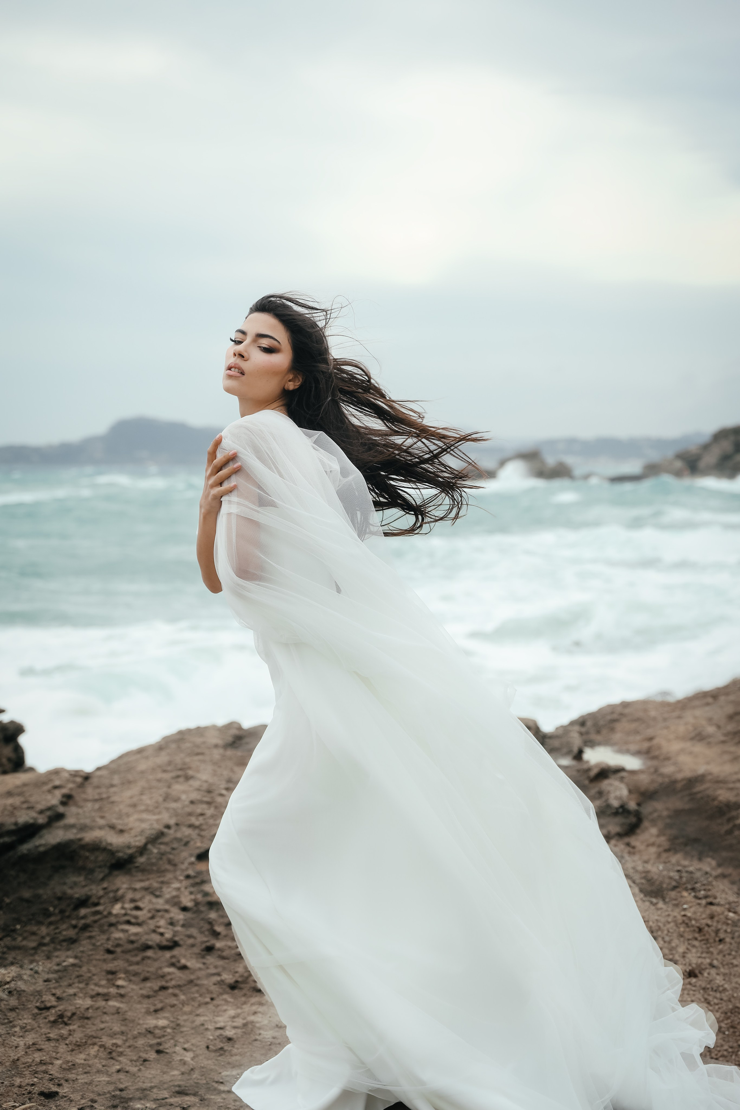 An art photo shoot of a girl in a wedding dress on the windy Kalithea beach in Rhodes, Greece