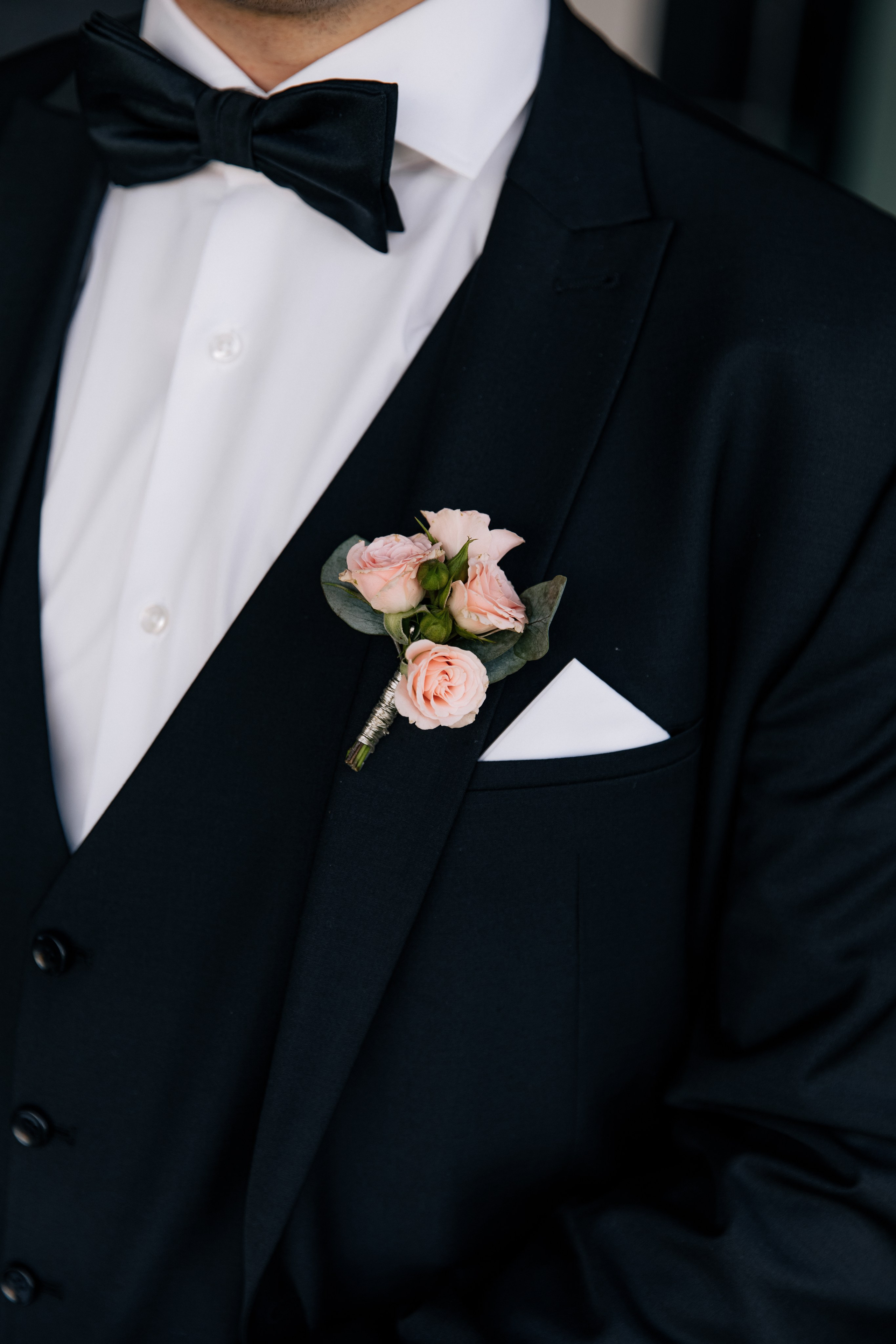 Details des Hochzeitsoutfits des Bräutigams: Boutonnière, Einstecktuch und Fliege. Elegante Accessoires, die den Look des Bräutigams vervollständigen.