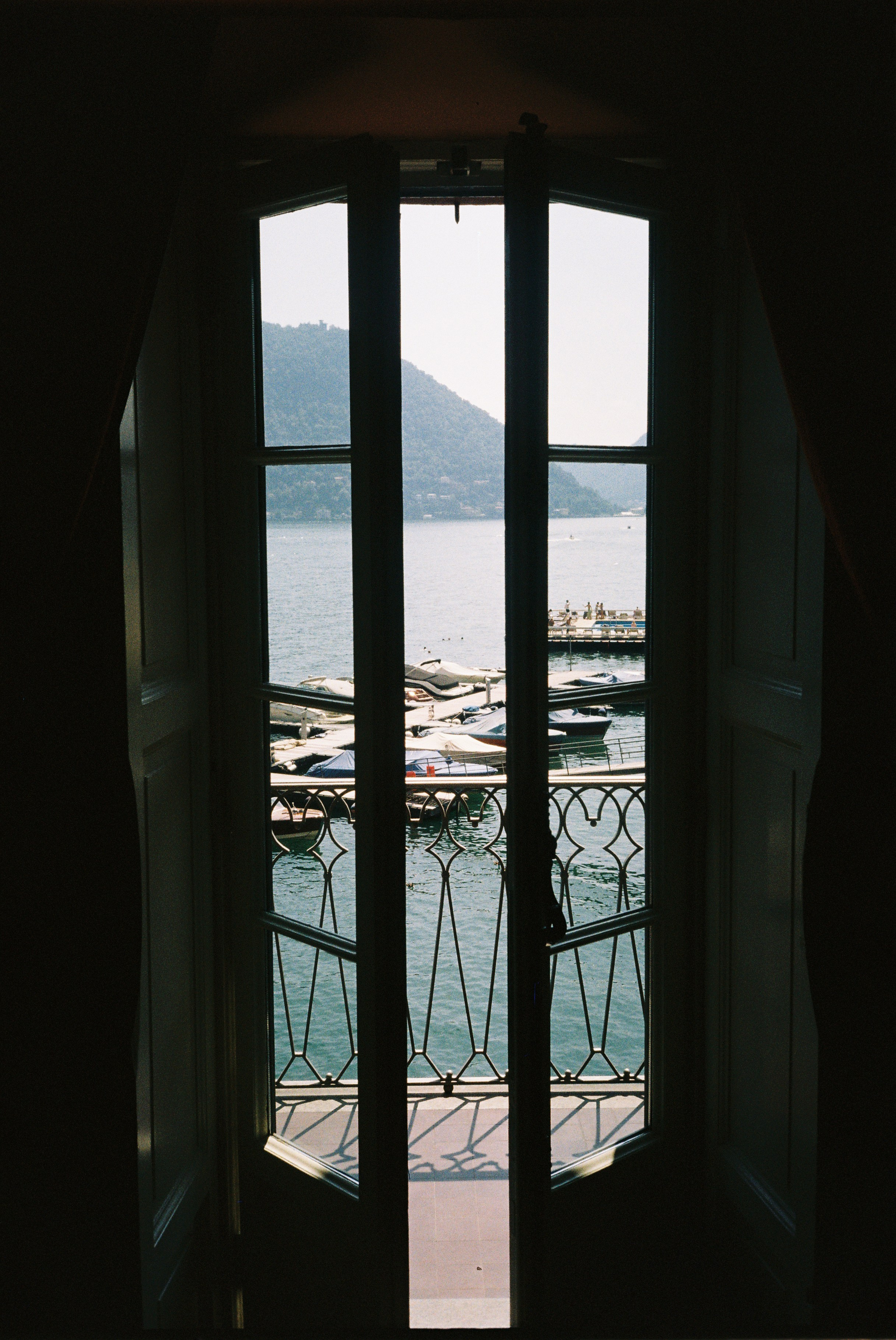Balcony view over a lake with boats, seen through open doors, capturing peaceful ambiance.