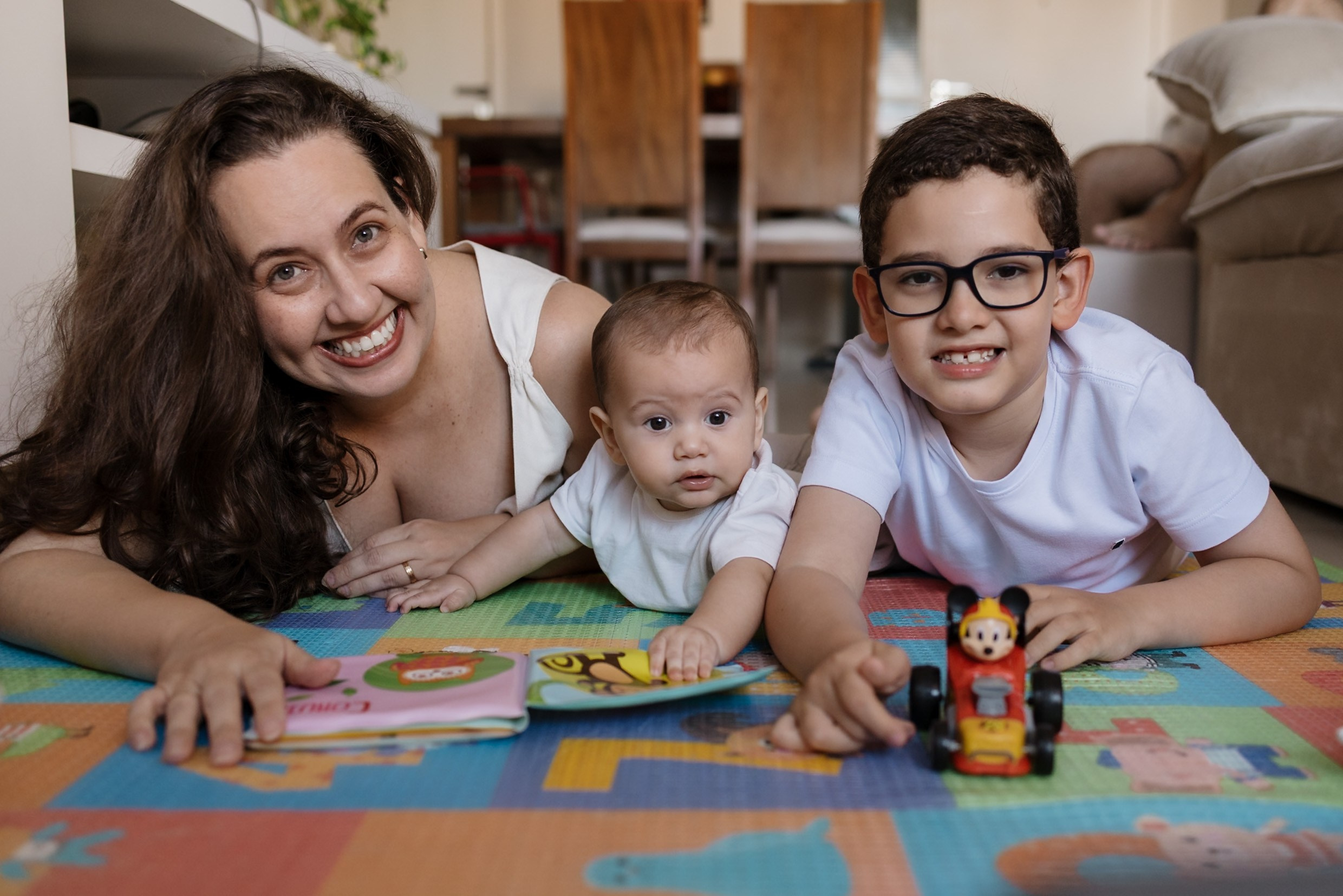 Irmão mais velho interage com o bebê no chão da casa.