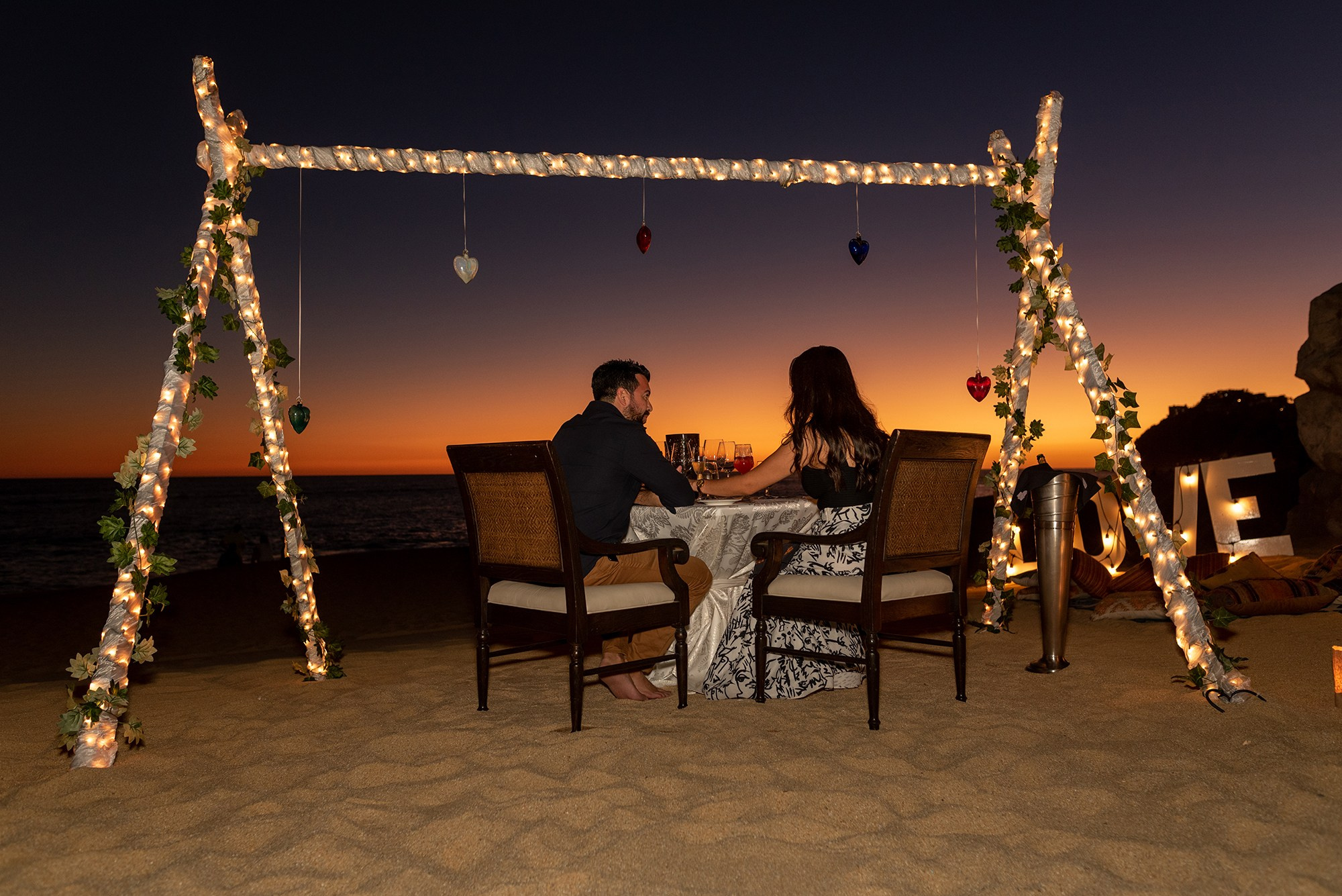Cabo San Lucas engagement session – newly engaged couple sitting under fairy lights after sunset proposal, romantic beach celebration photography
