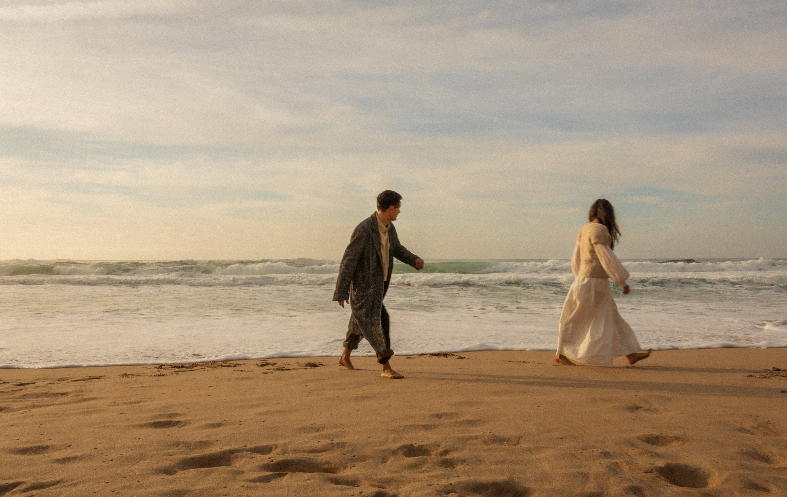 Couple holding hands and walking through a picturesque coastline in Portugal.