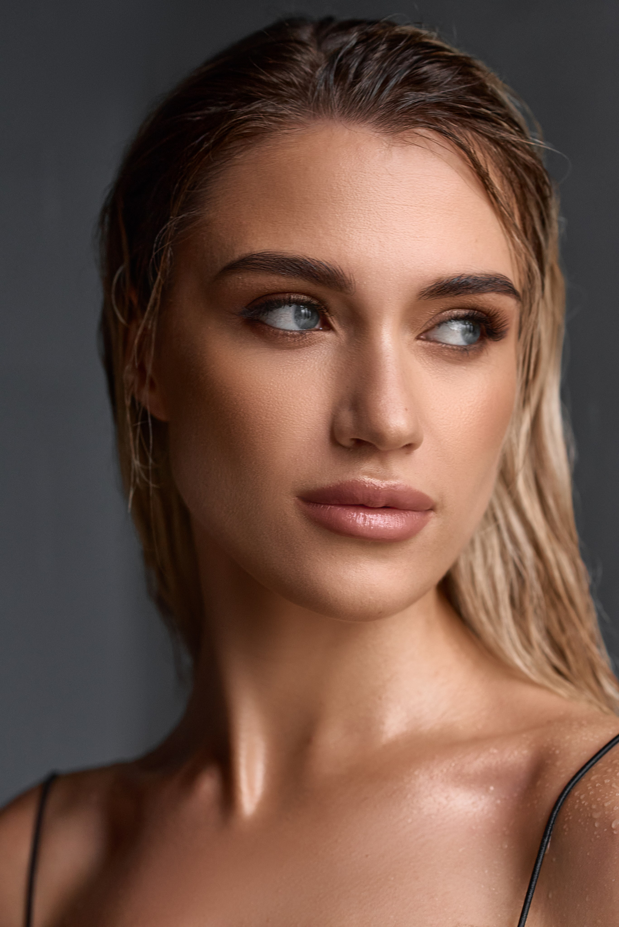 Жінка з мокрим волоссям після зйомки з водою. Її погляд відведений убік, а краплі води на шкірі додають ефекту натуральності та глибини образу.