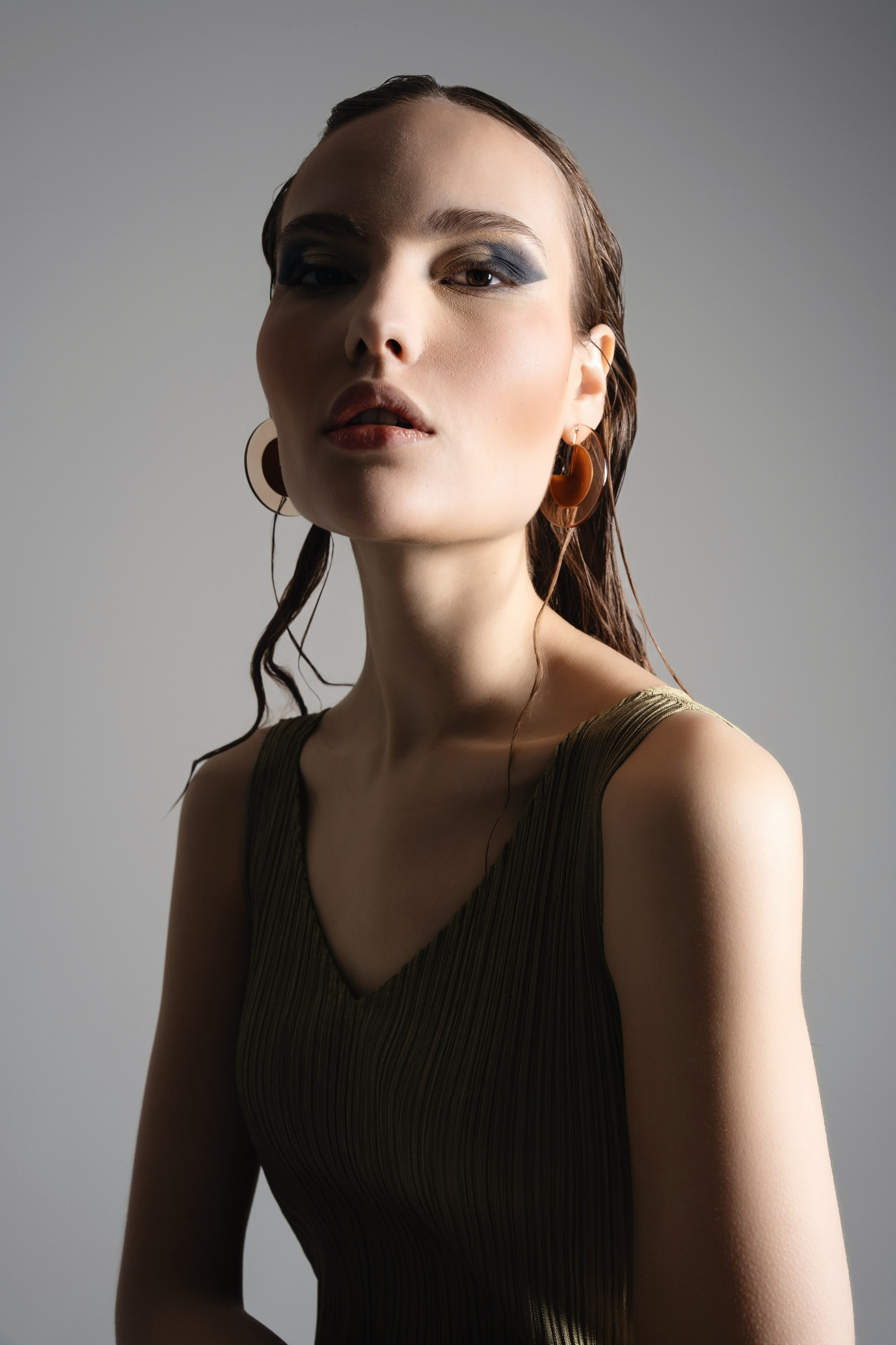 Studio portrait of a woman in a dark dress photographed against a neutral grey background in a refined fashion editorial style.