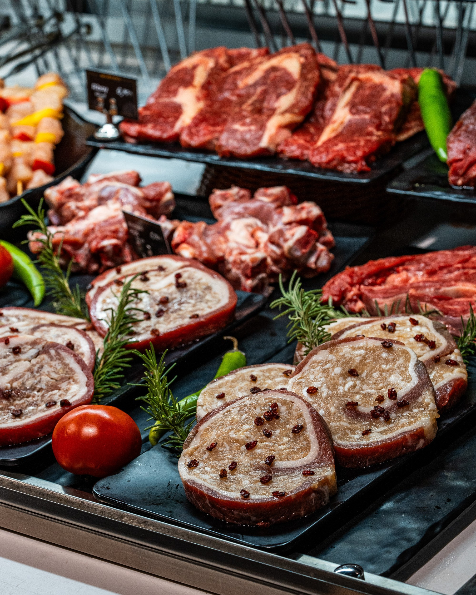 Qara tepsidə yerləşdirilmiş, üzərində qarağat dənələri (və ya bənzər ədviyyat) olan döş əti rulonları (ehtimal ki, mal və ya quzu), yanında rozmarin və pomidor.