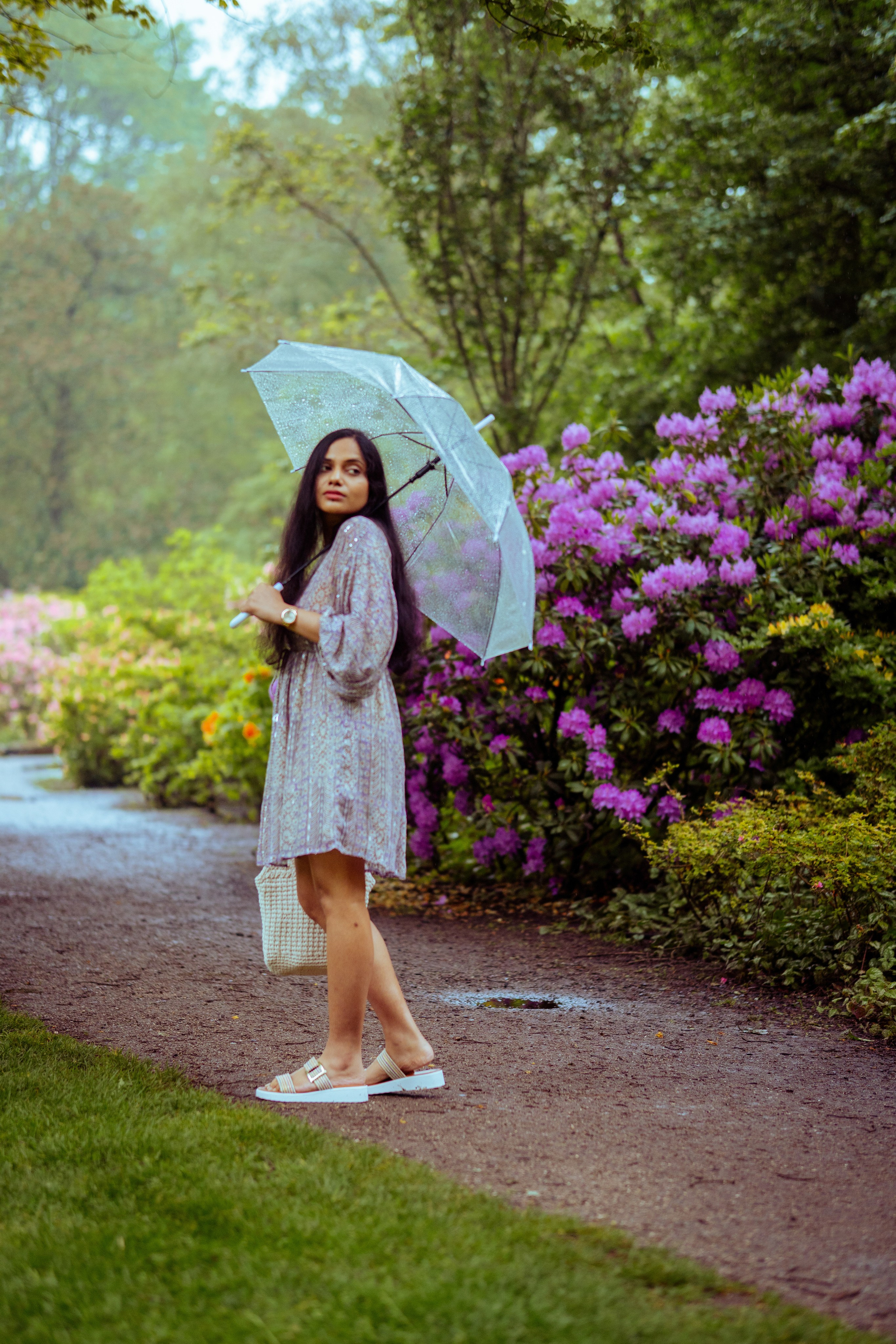 woman standing in a flower park and holding a transparent umbrella 