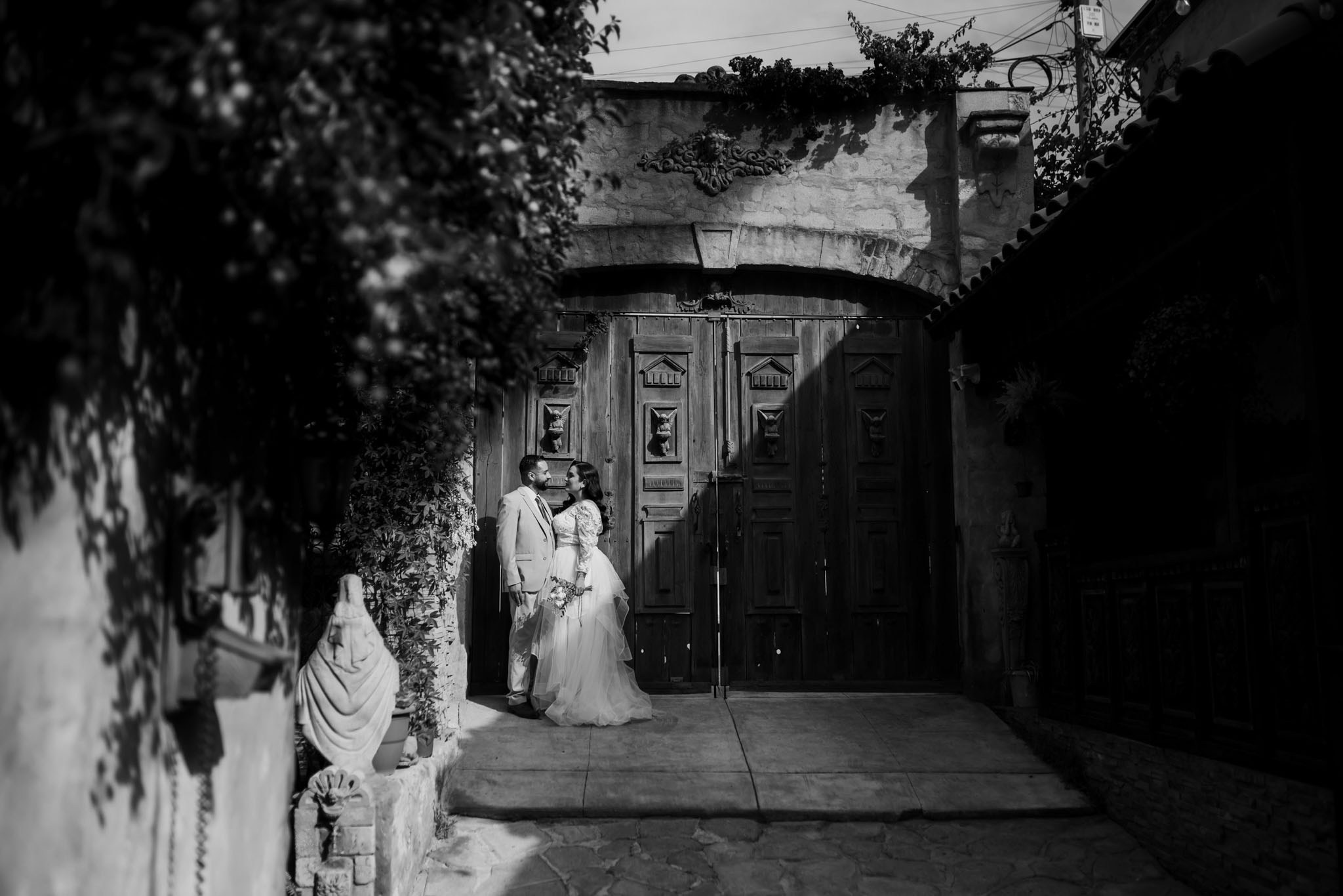 Fotografía de boda en blanco y negro en Tijuana, pareja de novios frente a portón en Jardín Casa Baga Rosarito, fotógrafo profesional de bodas estilo artístico y documental en Baja California