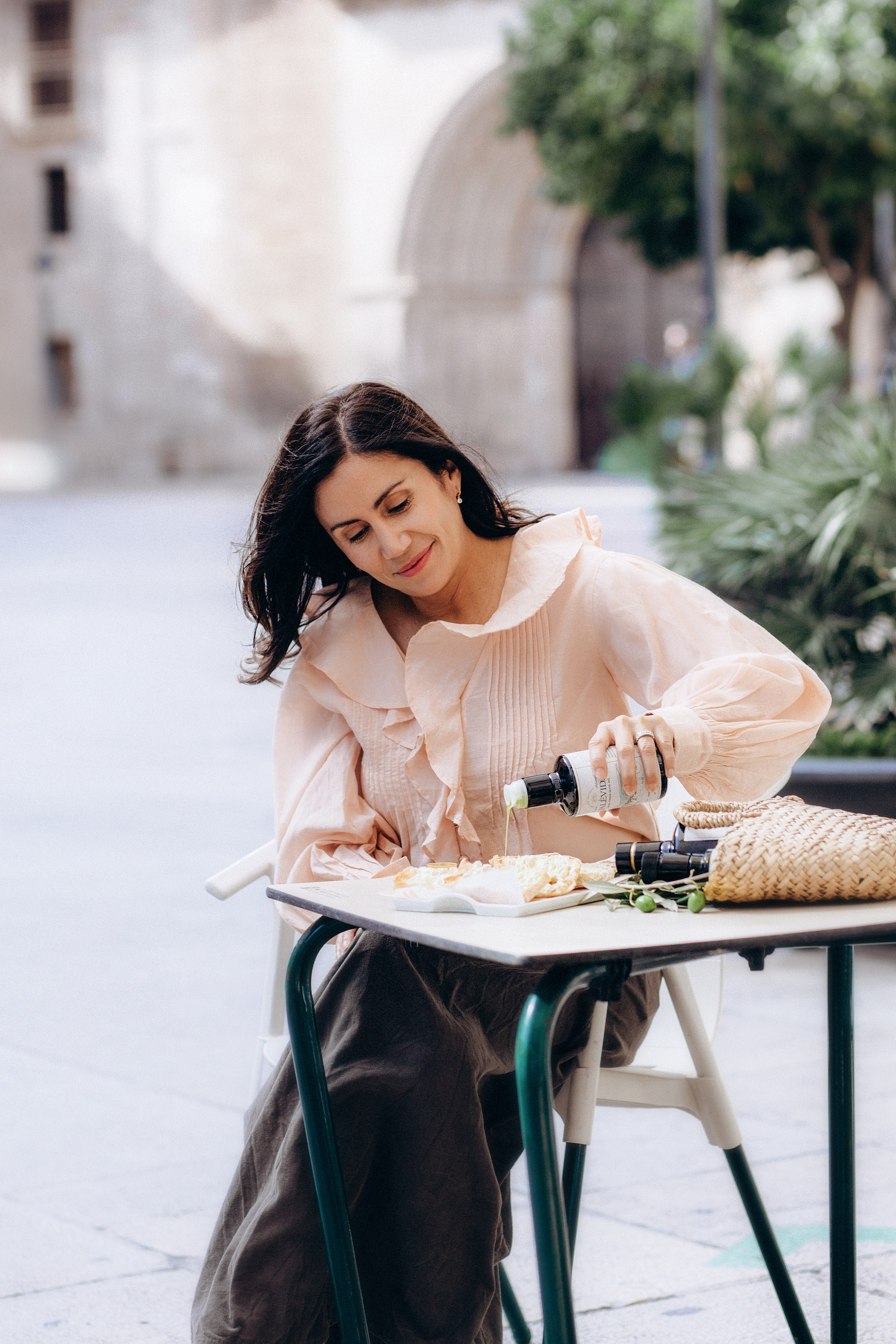 Lifestyle brand photoshoot in Valencia, Spain featuring a woman pouring olive oil at an outdoor café table — perfect for showcasing authentic product use in content and product photography for Mediterranean or artisanal brands.