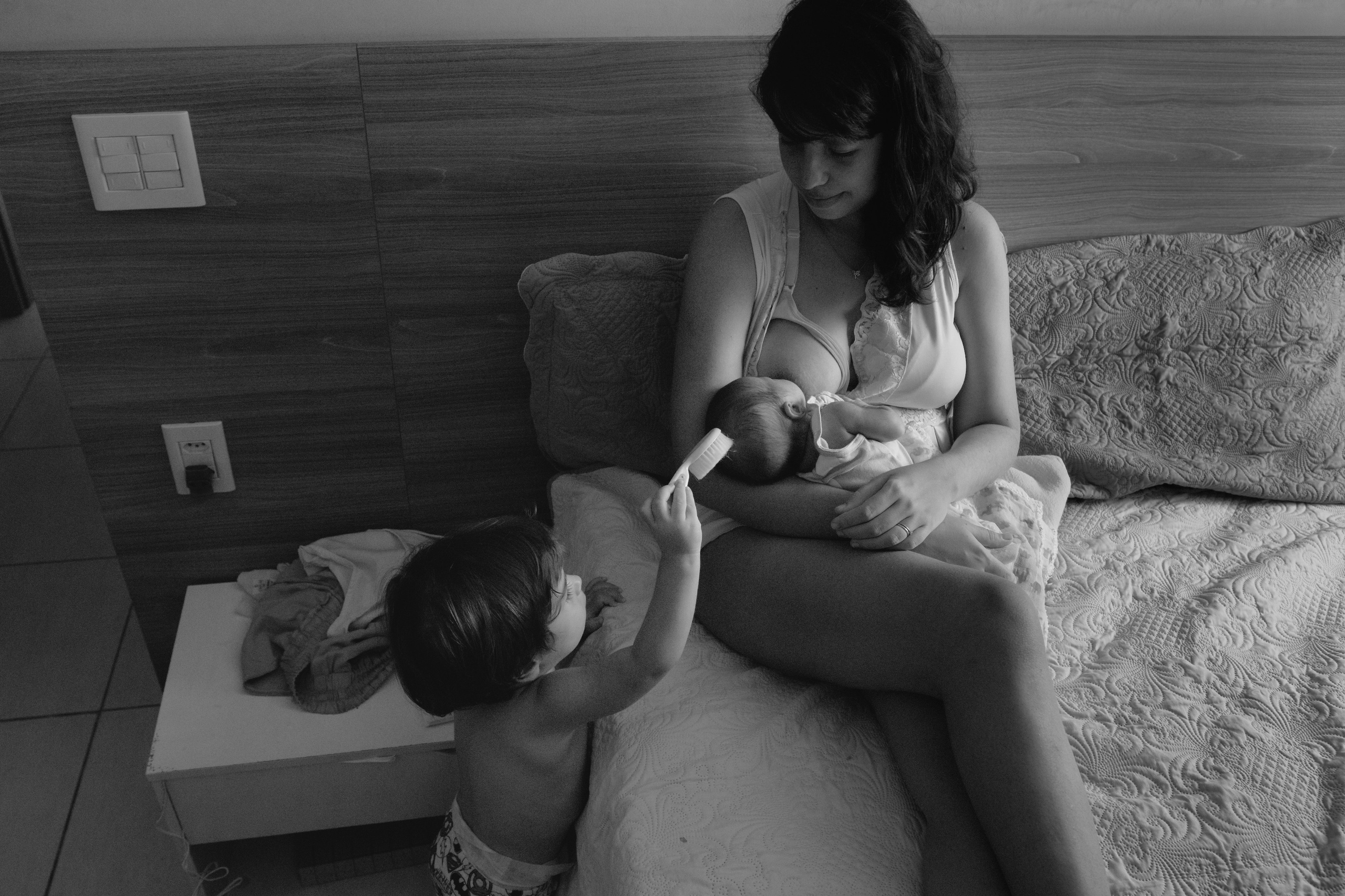 Criança escovando o cabelo da irmã recém-nascida enquanto a mãe amamenta