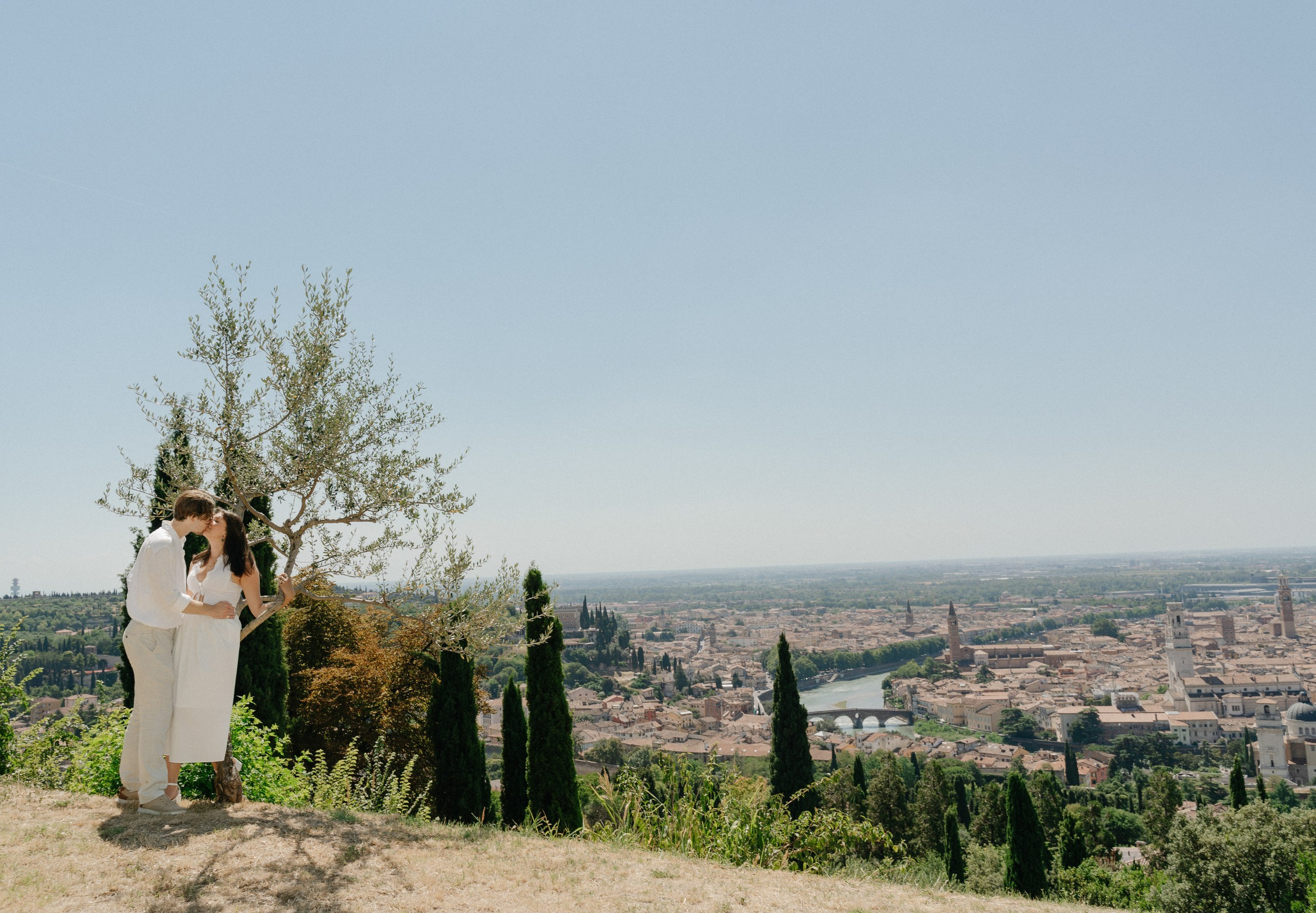Couple embracing after a surprise marriage proposal with Verona's historic center in the background.