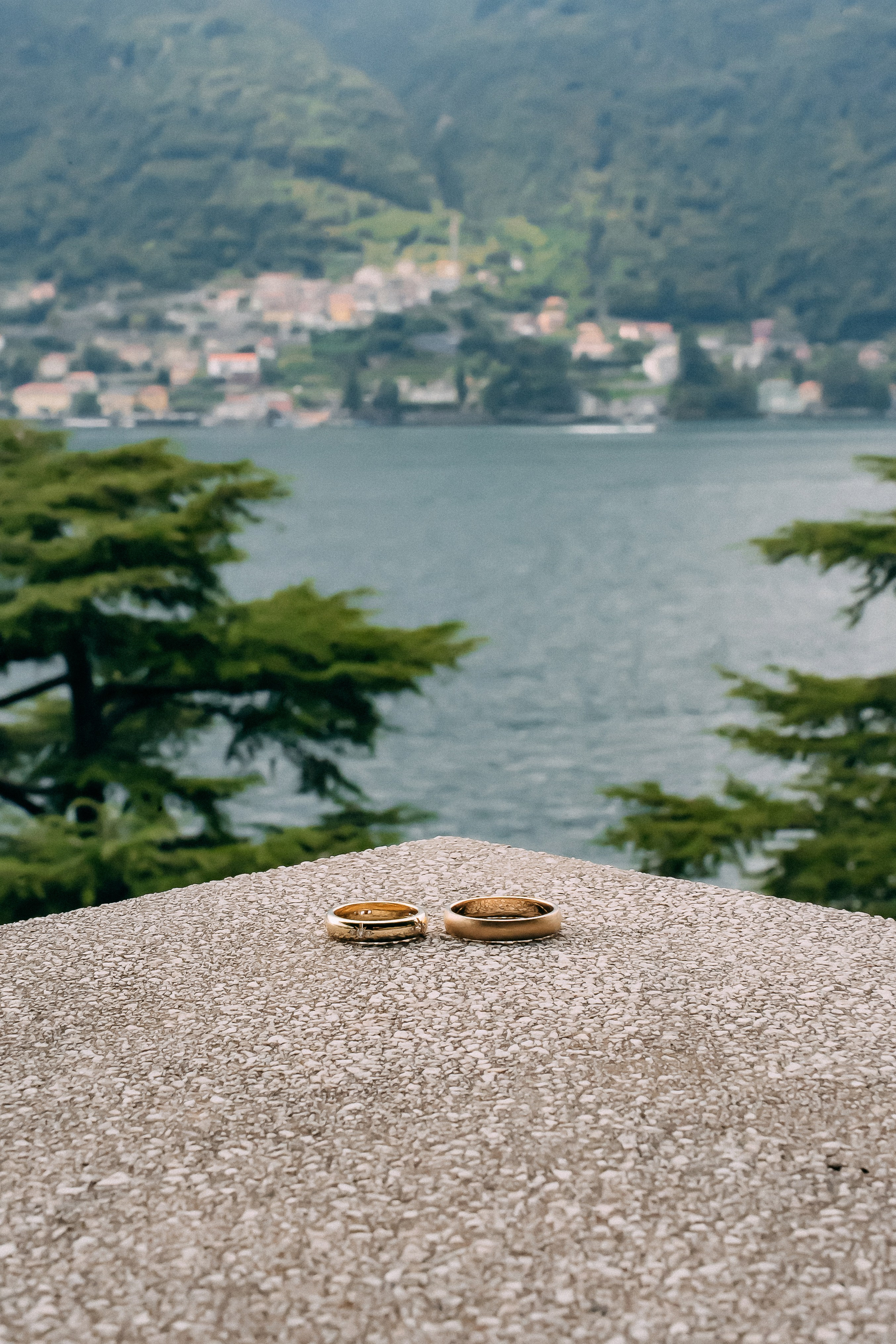 Wedding rings resting on the pebble shore of Lake Como with village view, Italy