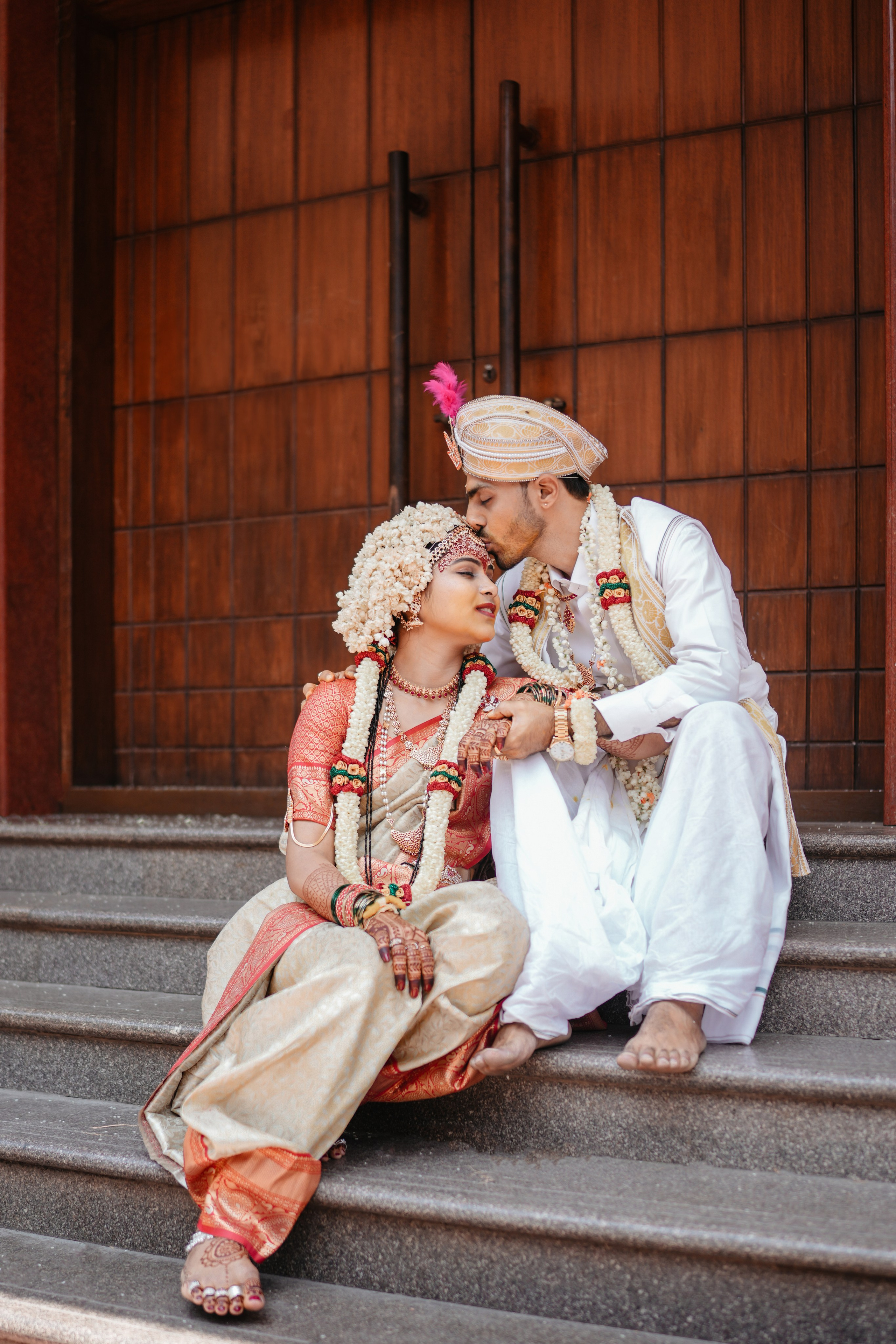 professional outdoor candid photo of a newlywed South Indian couple sitting on steps, groom kissing bride's forehead, in Malleshwaram, Bengaluru