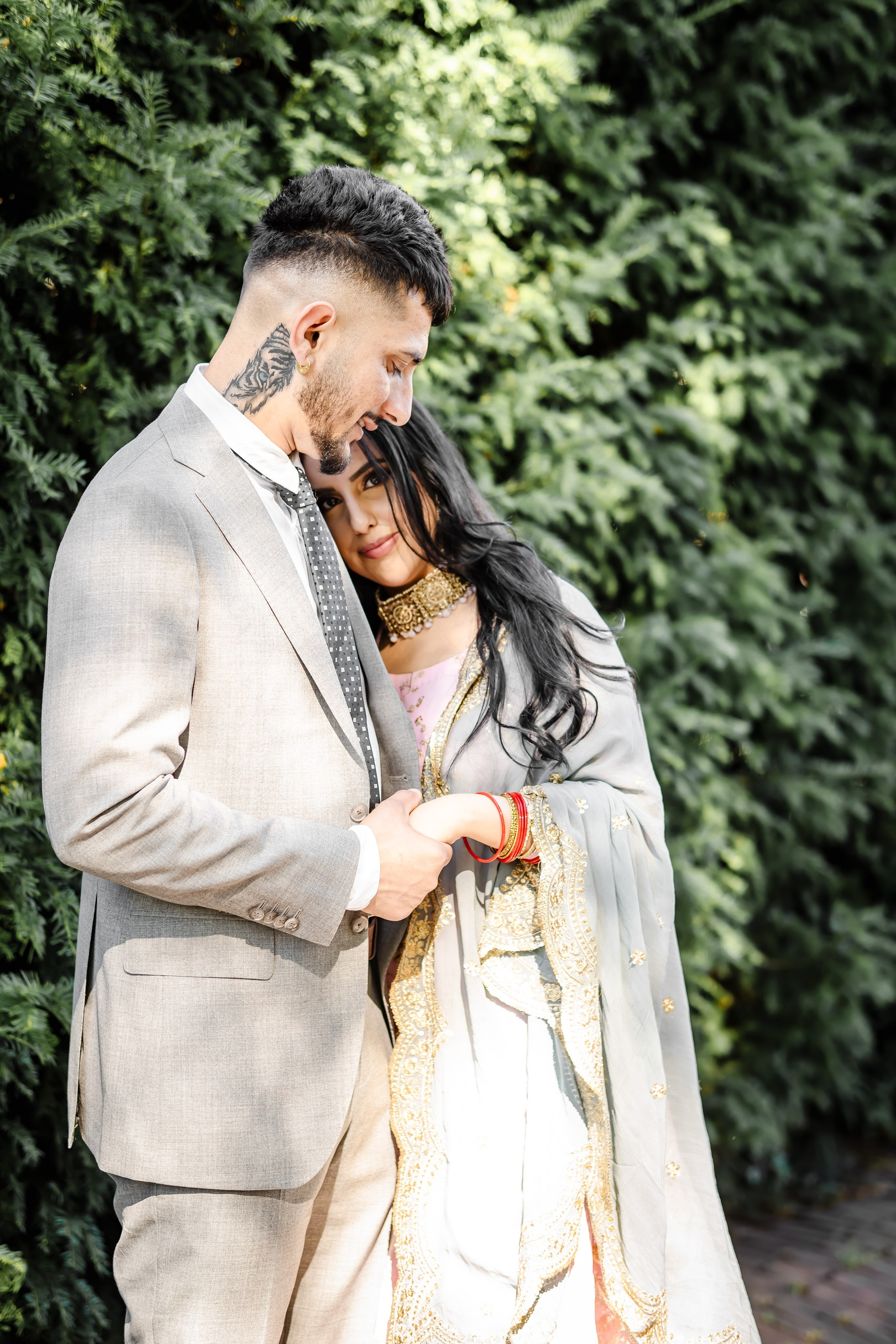 a woman wearing lehenga leaning on the chest of a man wearing a grey suit 