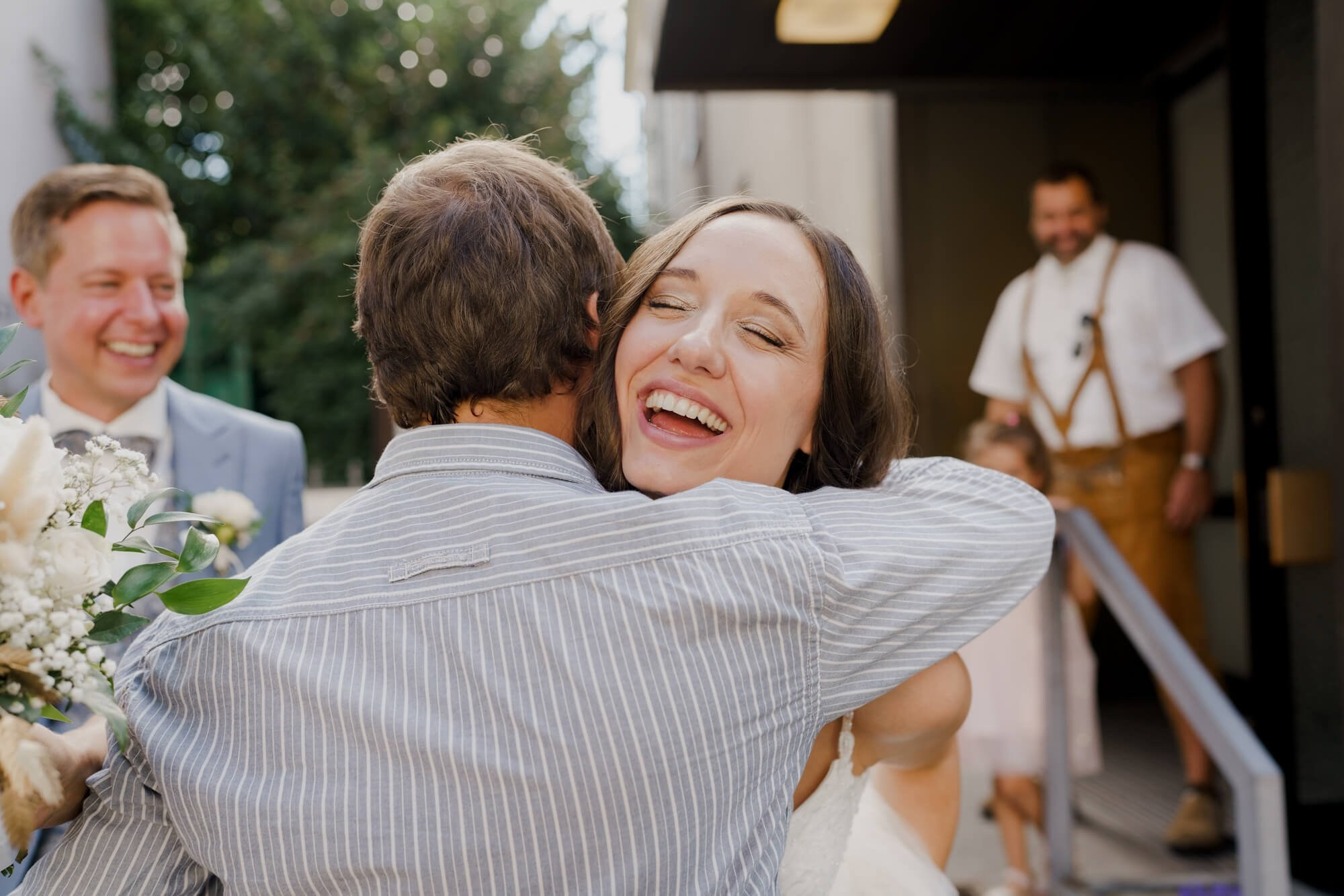 Bride laughing and embracing a guest outside the venue immediately after the Stuttgart wedding ceremony, bouquet still in hand