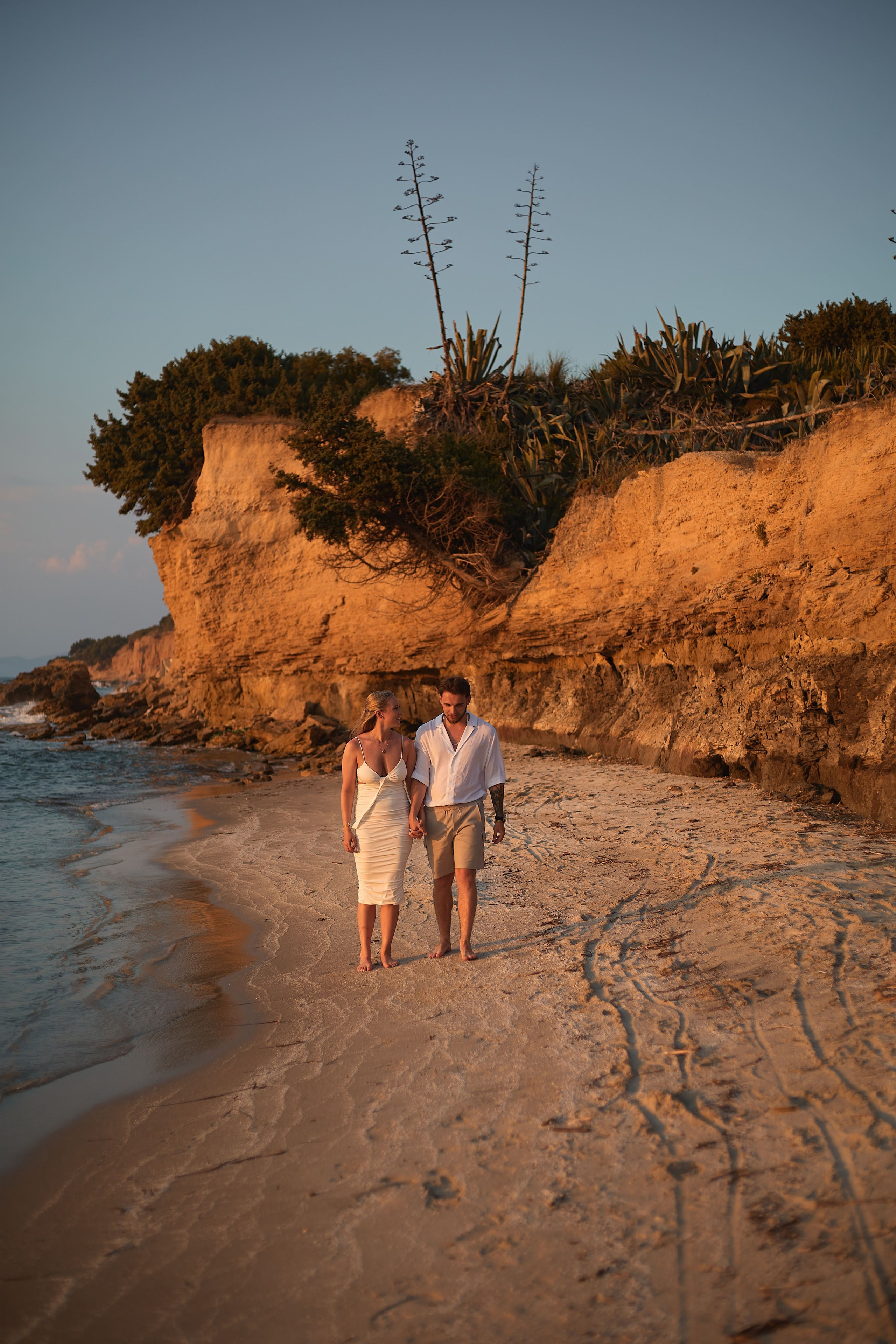 Couple in love walking on the beach in Greece holding hands during sunset