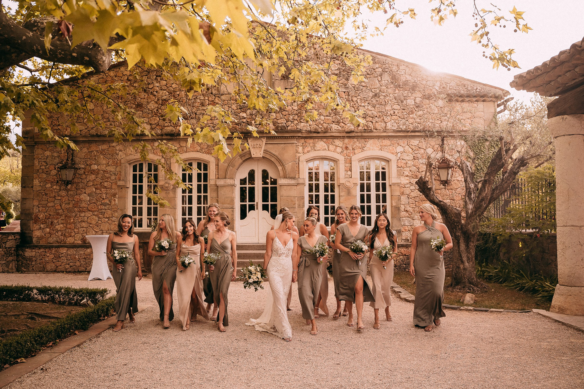 A vibrant group shot of the bride leading her bridesmaids in a lively walk toward the camera, their dresses flowing as they smile under the golden afternoon light.