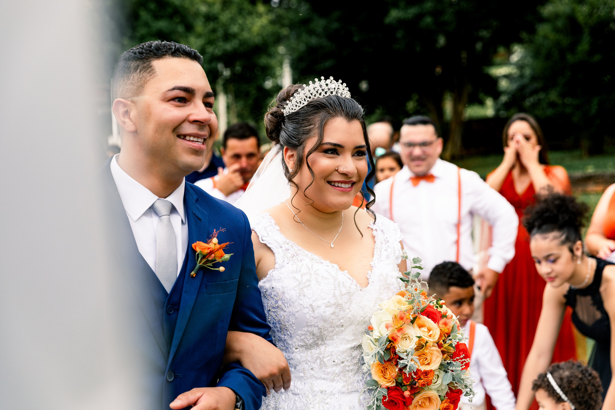 Noivos de mãos dadas durante a cerimônia de casamento, concentrados na fala do celebrante.