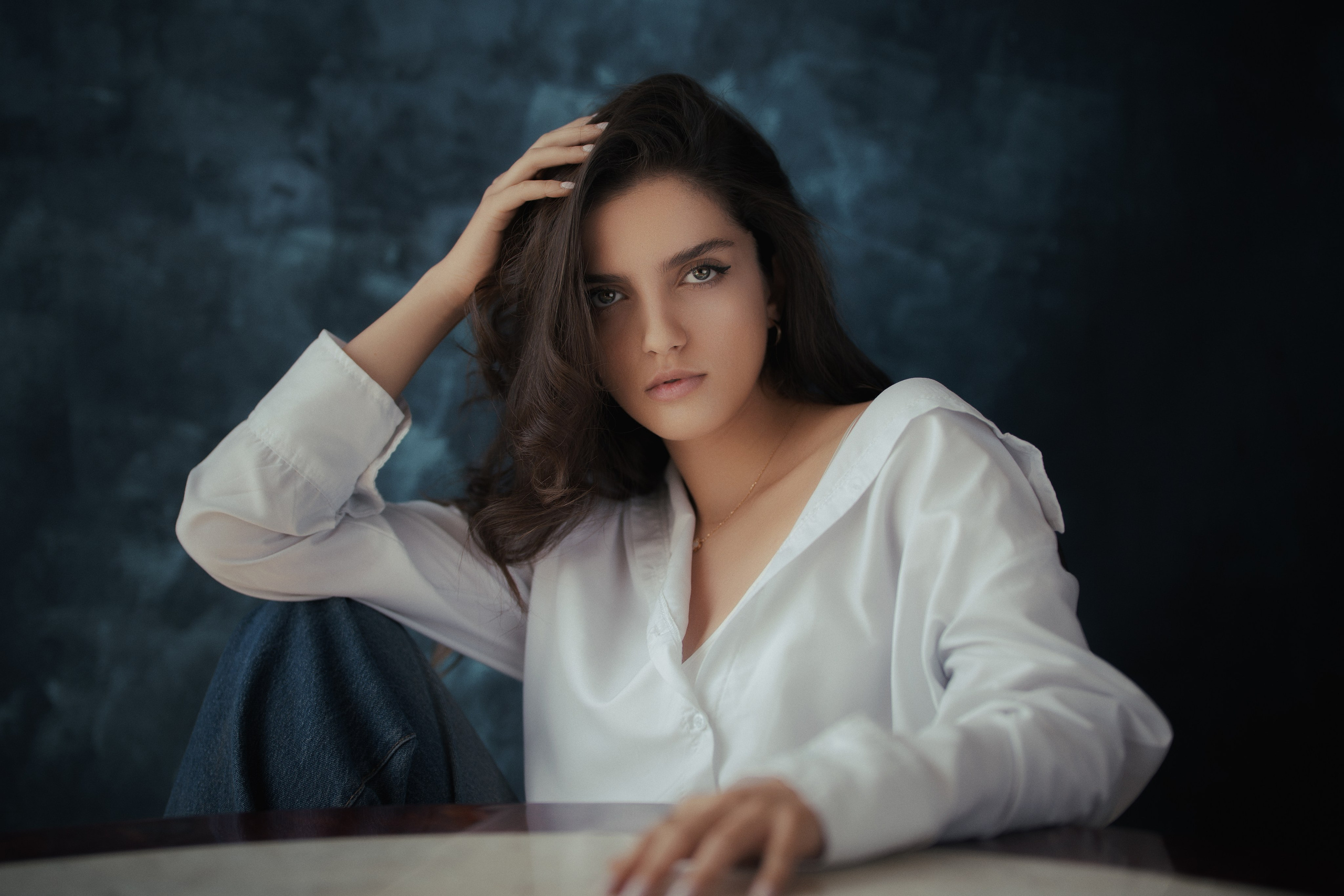 Elegant female portrait photography by Mehran Hadad featuring a young woman in a white shirt with cinematic studio lighting, a textured blue backdrop, and timeless fine art styling.