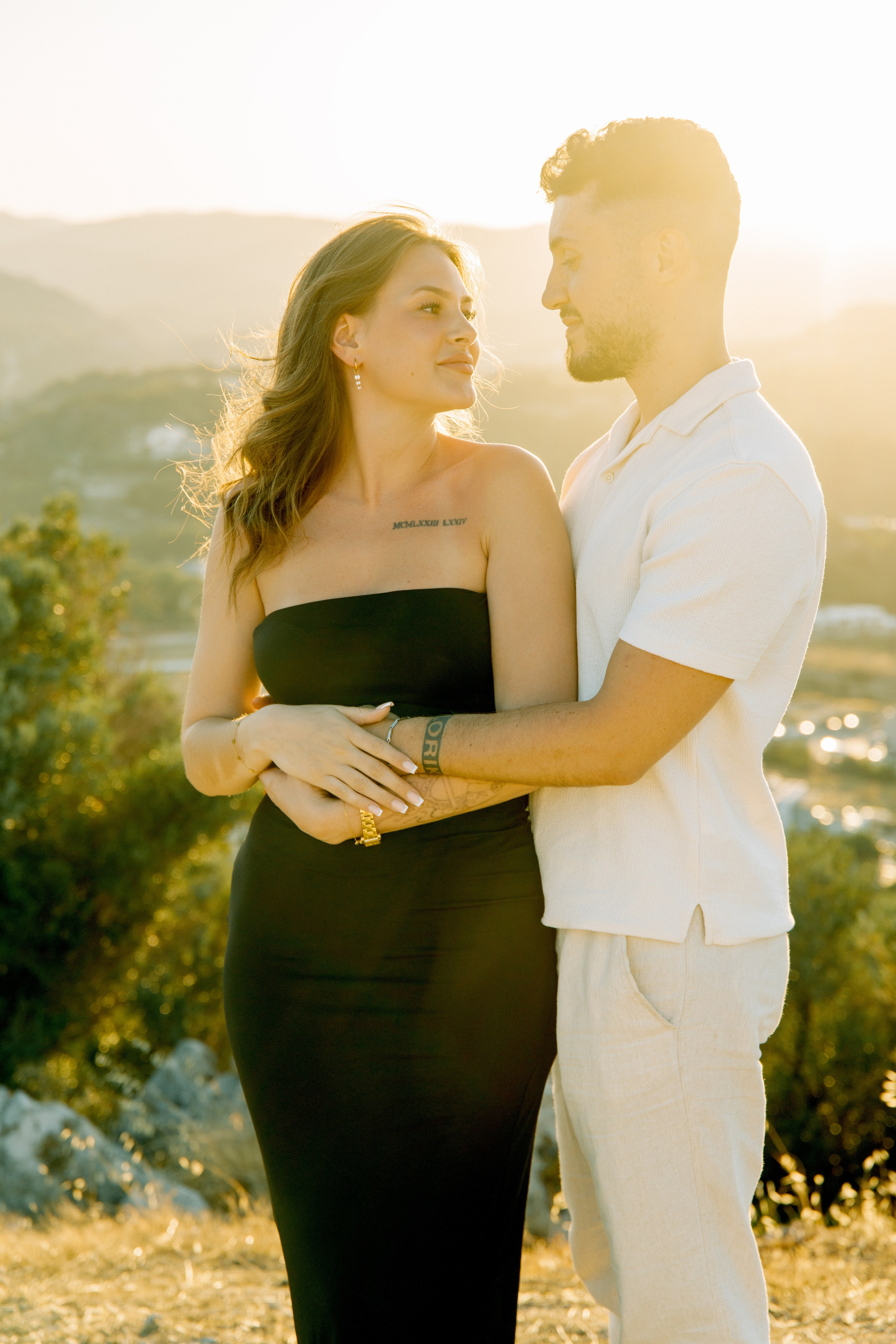 "Liebevoller Blickkontakt: Ein Paar auf dem Felsplateau des Profitis Ilias vor der Kulisse von Faliraki und dem Mittelmeer."