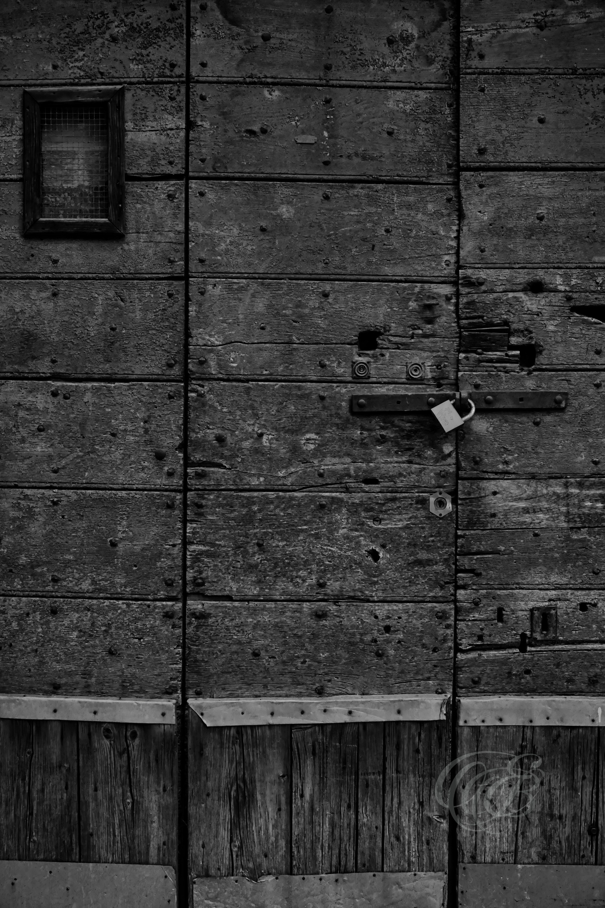Street Photography — Rome, Italy — Old Reclaimed Wood Door — B&W — Black and white study of a Roman door made from reclaimed wood, emphasizing aged timber, irregular textures, traditional reuse, and traces of the material’s earlier history — Eduardo Bartoli Photography.