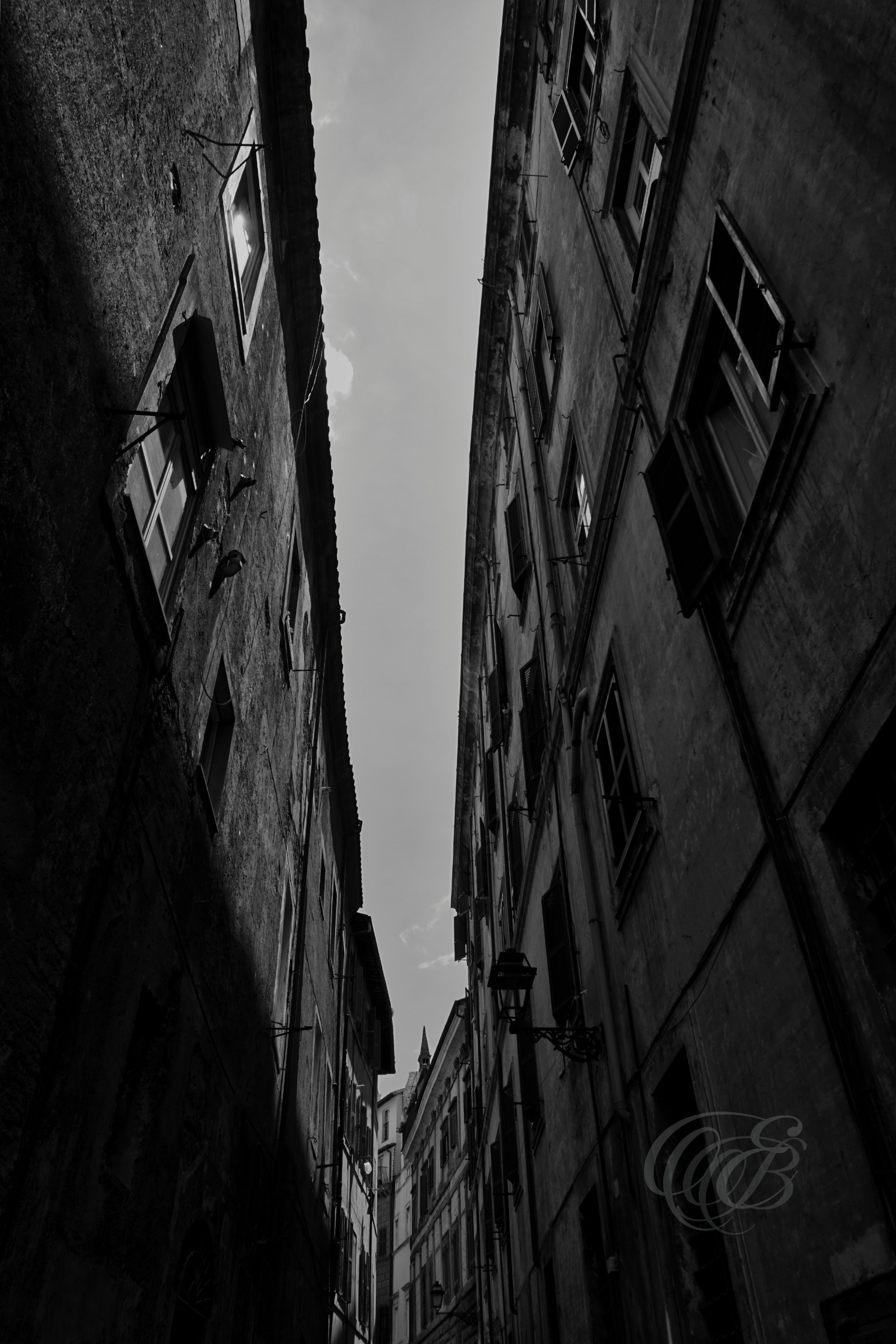 Street Photography — Rome, Italy — Narrow Street — B&W — Black and white view of a narrow Roman street, emphasizing perspective, architectural textures, light and shadow, and the intimate scale of the city’s historic urban fabric — Eduardo Bartoli Photography.