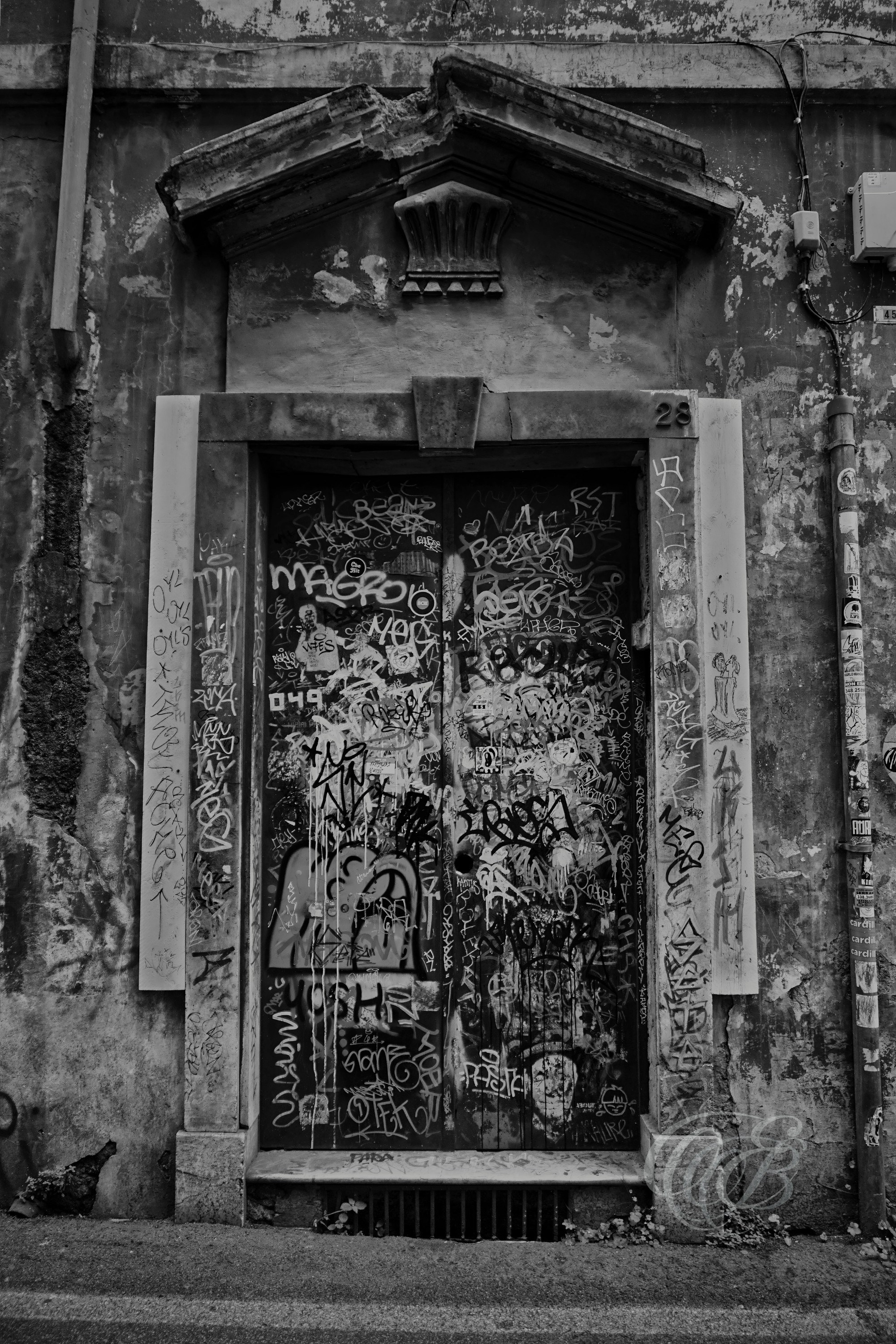 Street Photography — Rome, Italy — Door Covered in Graffiti — B&W — Black and white study of a graffiti-covered door in Rome, emphasizing urban textures, contemporary street expression, weathered surfaces, and the contrast between old architecture and modern markings — Eduardo Bartoli Photography.