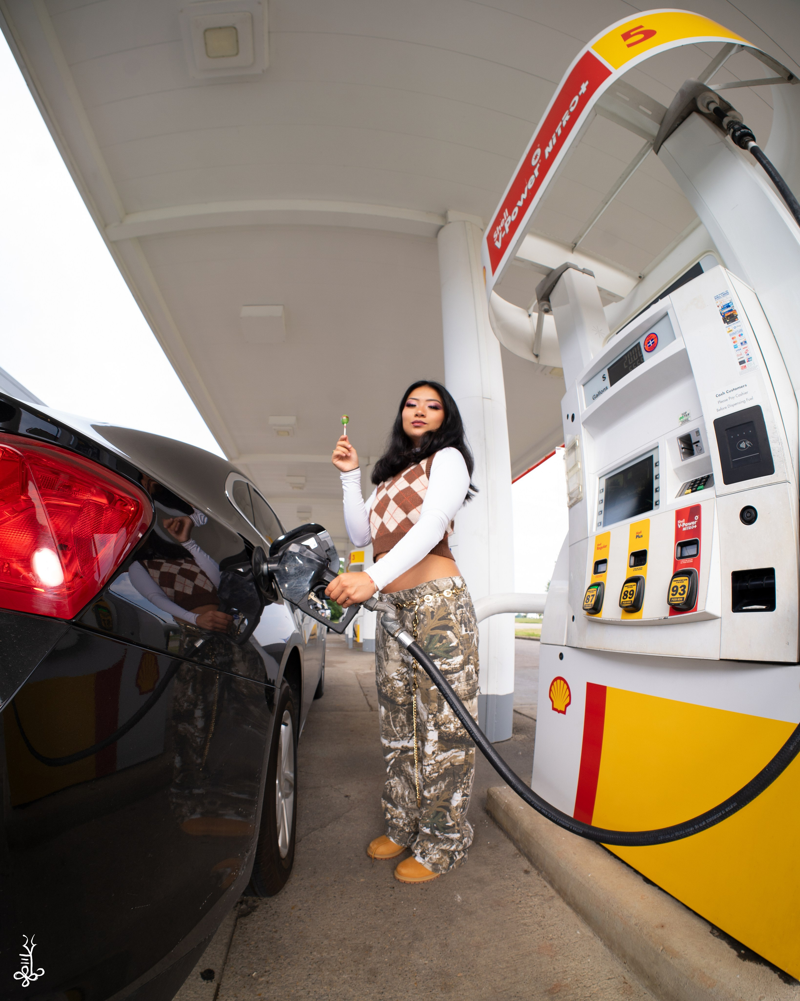 Model smiling while pumping gas wearing brown and white argyle sweater vest