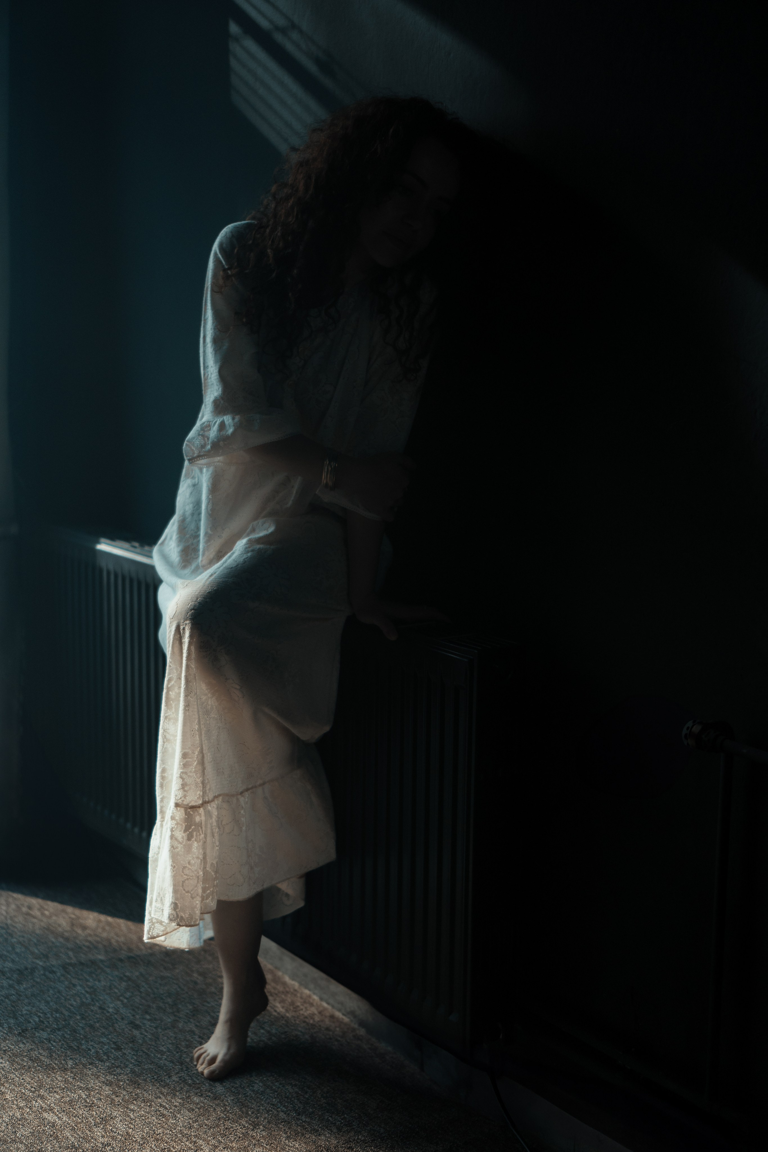 Künstlerische Fotografie – Frau im weißen Kleid steht im Halbdunkel, geheimnisvolle Stimmung