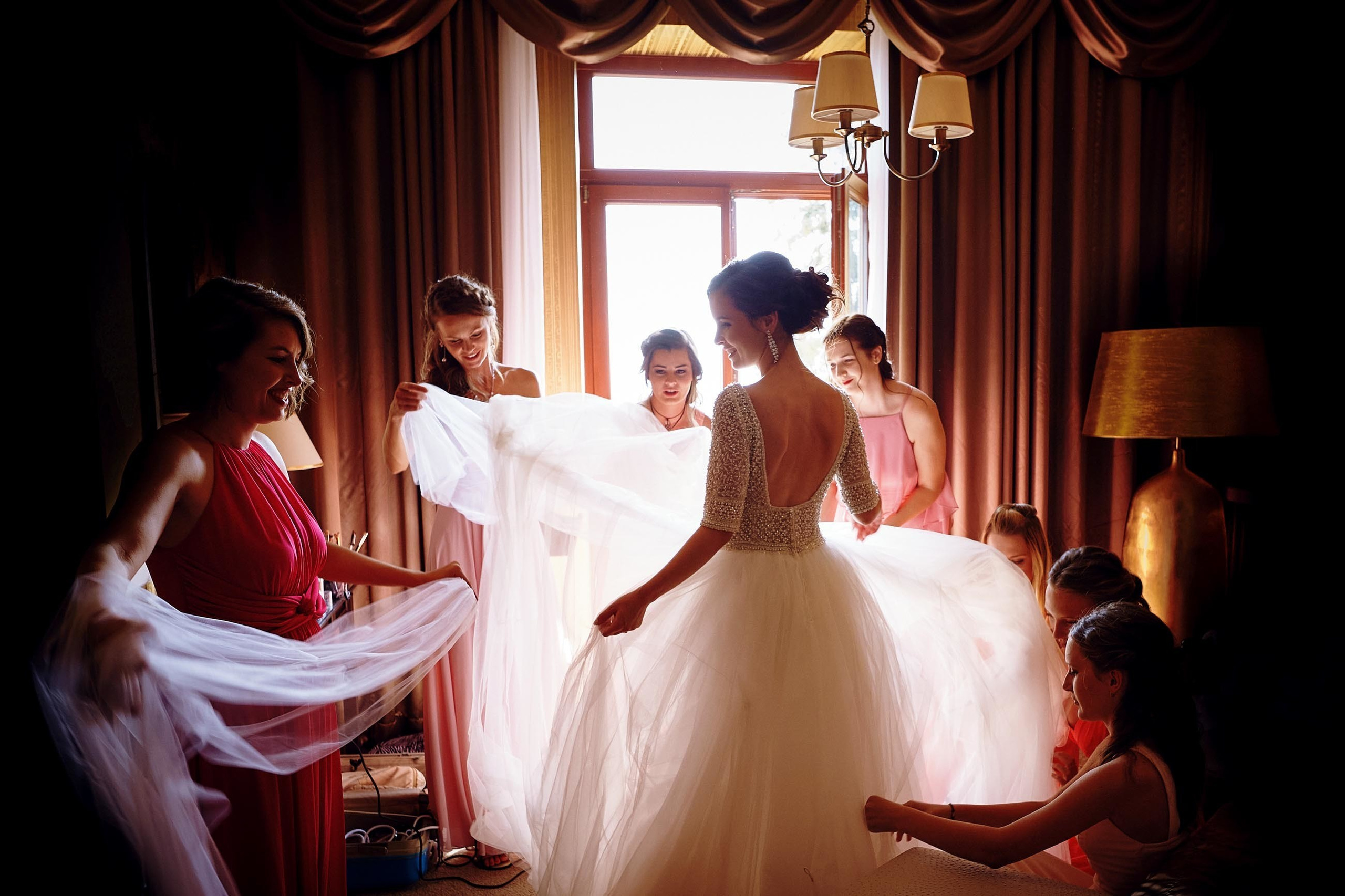 Silhouetted bride with bridesmaids adjusting her dress, preparing for destination wedding at Grand Tatras, Slovakia.