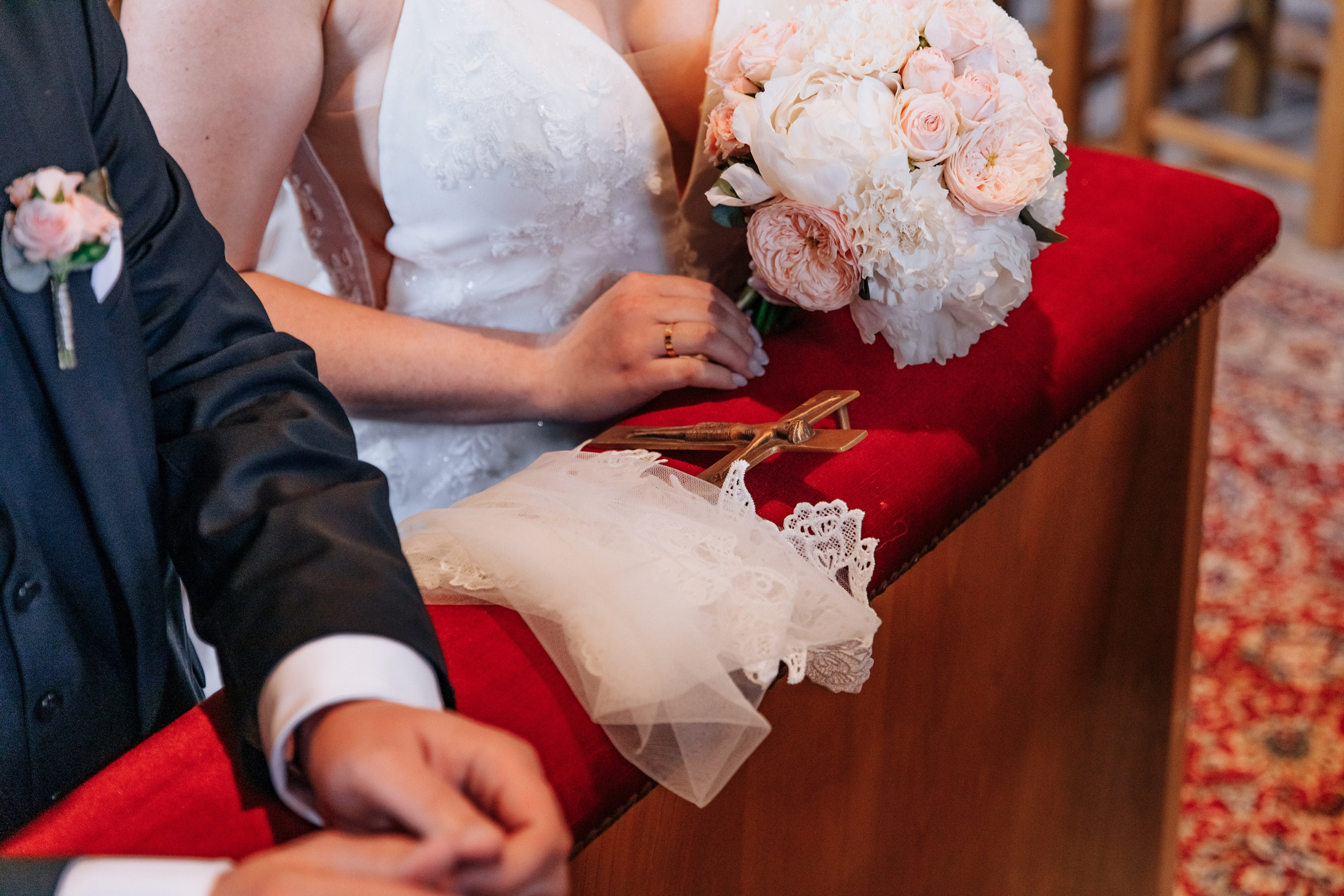 Die Hände der Braut halten den Brautstrauß, ein Taschentuch und ein Kreuz.