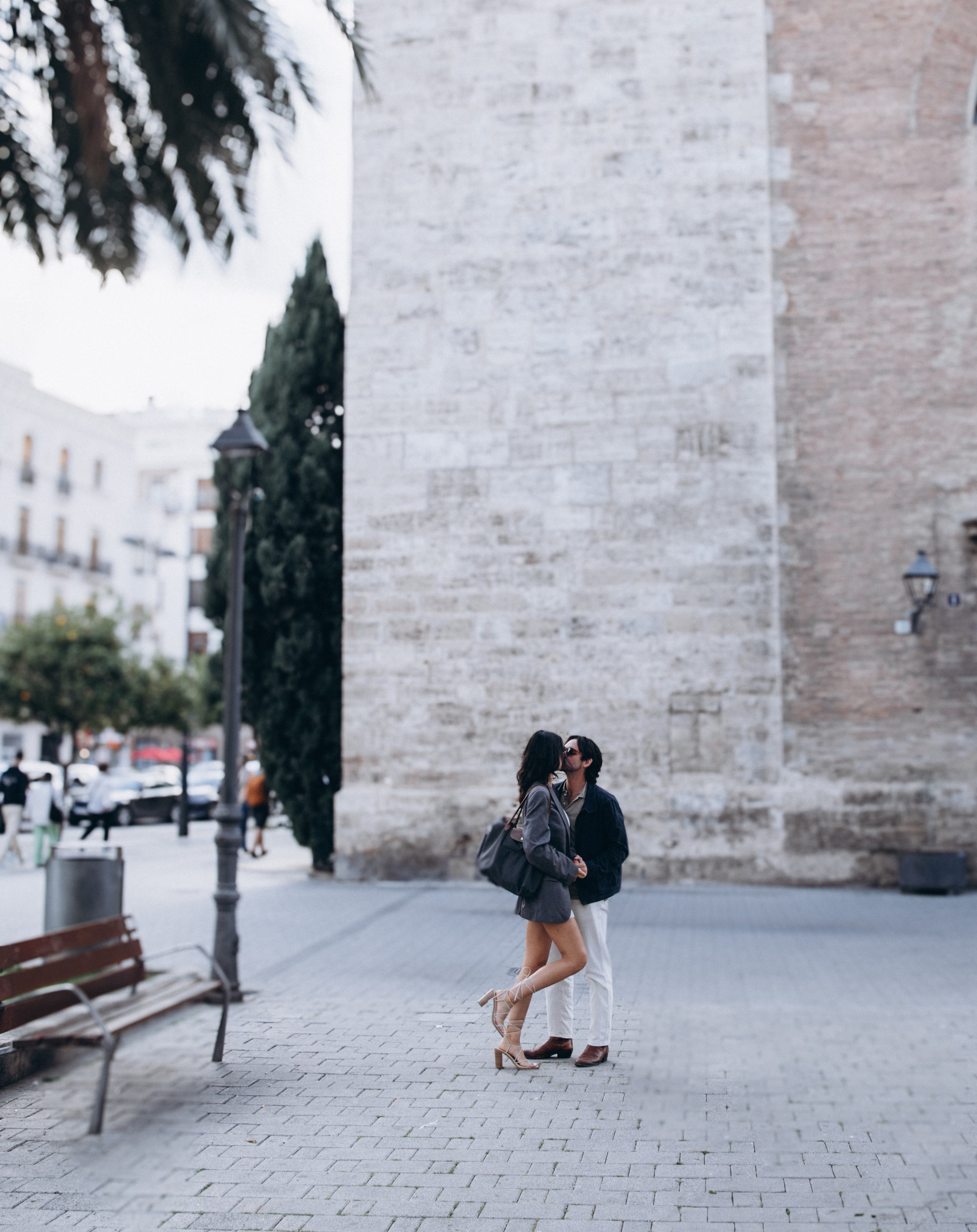 Romantic outdoor portrait of a couple sharing a sweet moment in front of a historic stone wall in Madrid, Spain — candid love story photography capturing intimacy, architecture, and spontaneous affection, perfect for couple photoshoots in Madrid and across Spain.