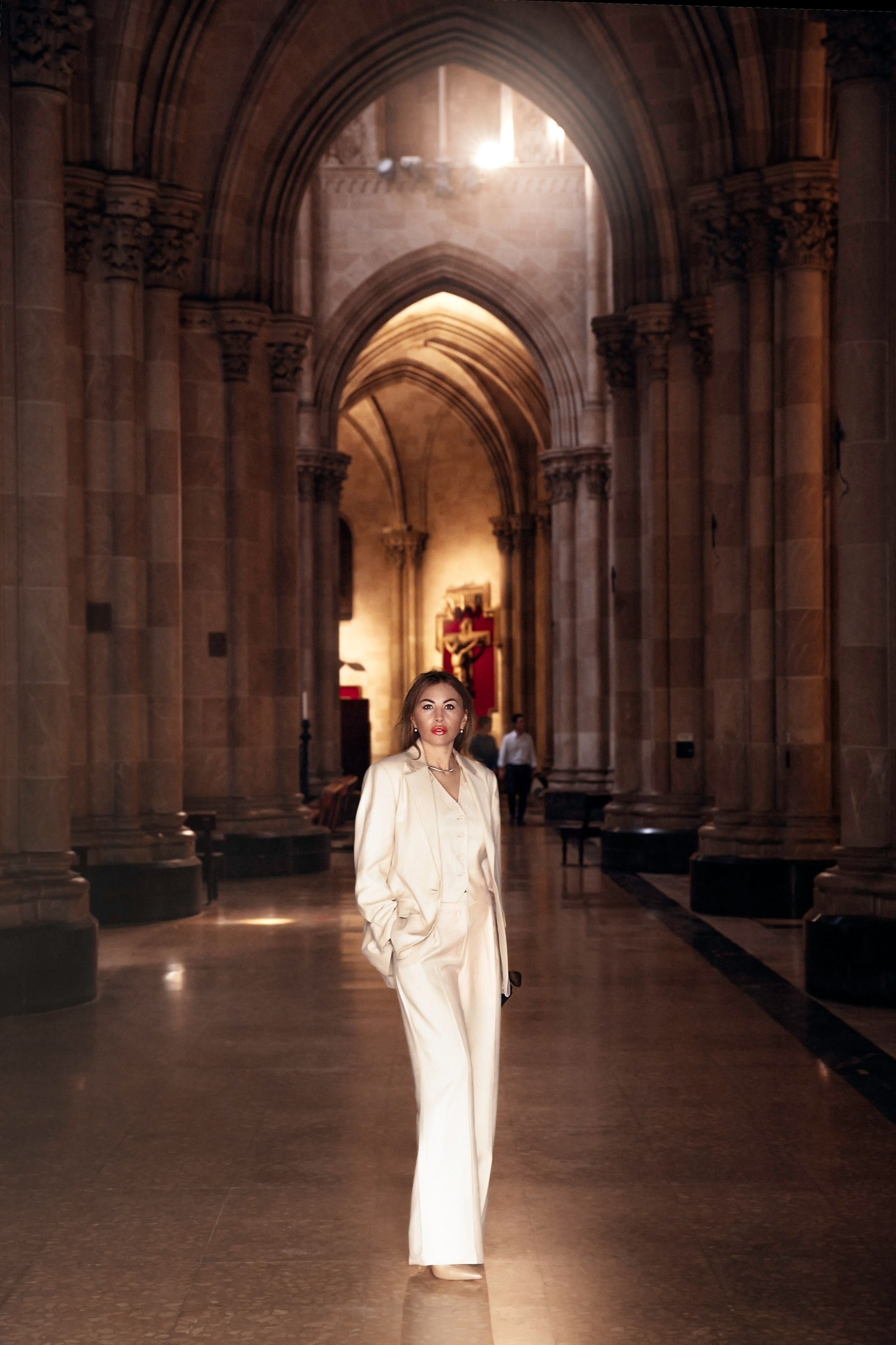 Элегантная женщина в стильном кремовом костюме, стоящая в главном проходе готического собора, с изысканными каменными арками и атмосферным освещением, в Валенсии, Испания