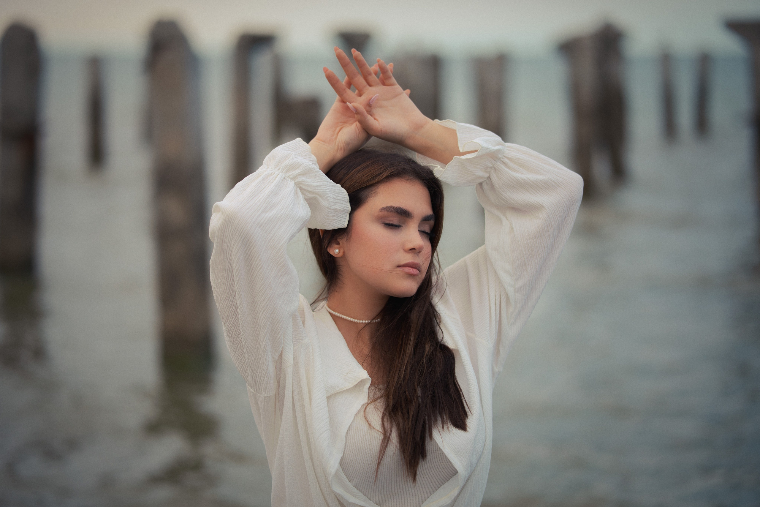 Outdoor female portrait photography by Mehran Hadad with a fashion-inspired pose, soft natural light, and cinematic seaside background.
