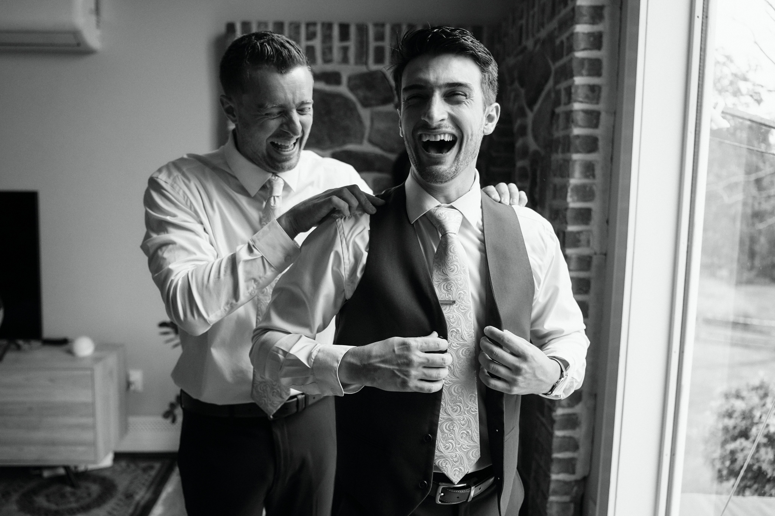 Black and white candid photo of groom getting ready with groomsman at New York wedding
