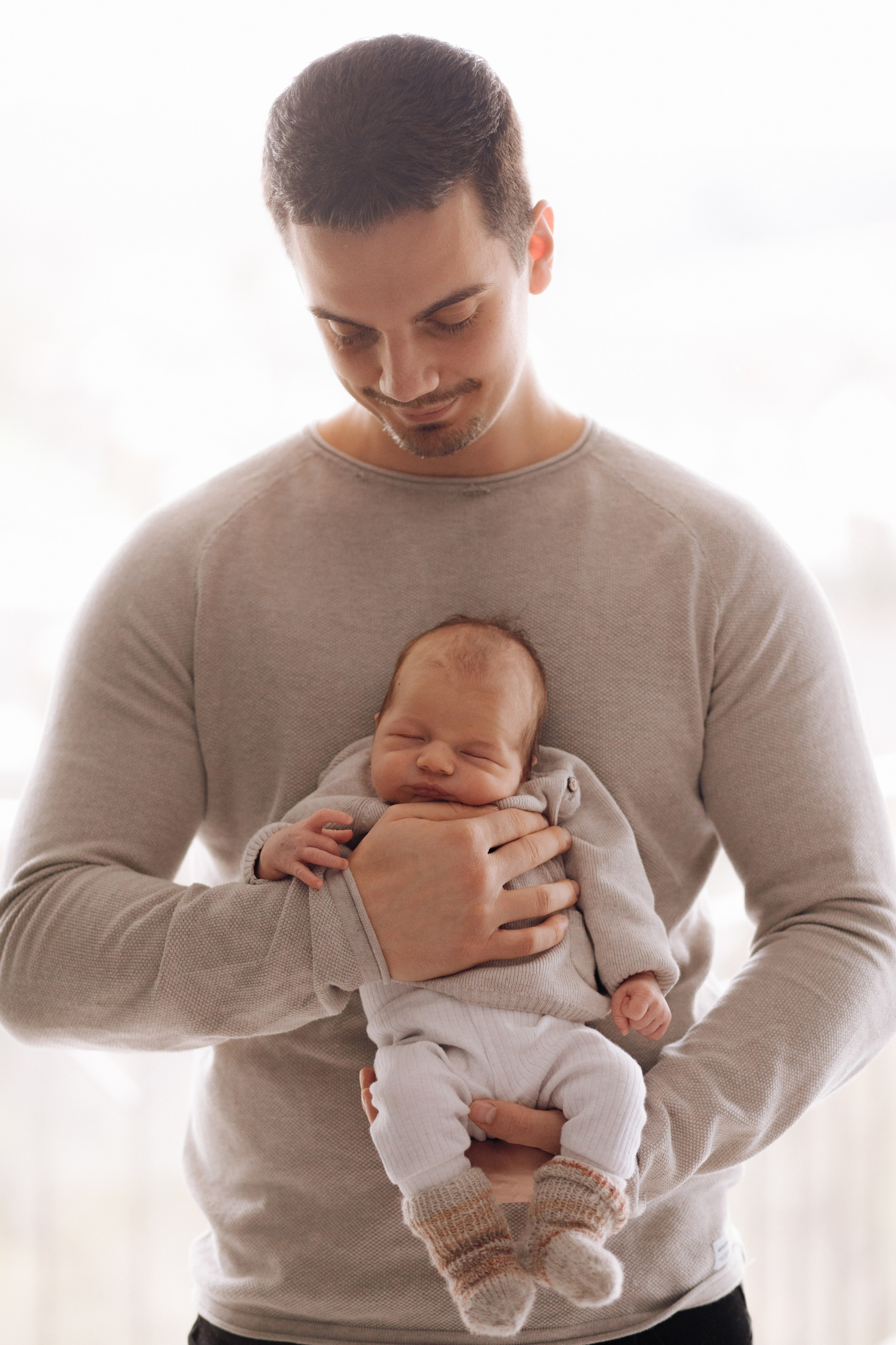 Papa hält das Neugeborene sanft und zugleich sicher in seinen Armen während eines liebevollen Neugeborenen-Fotoshootings.