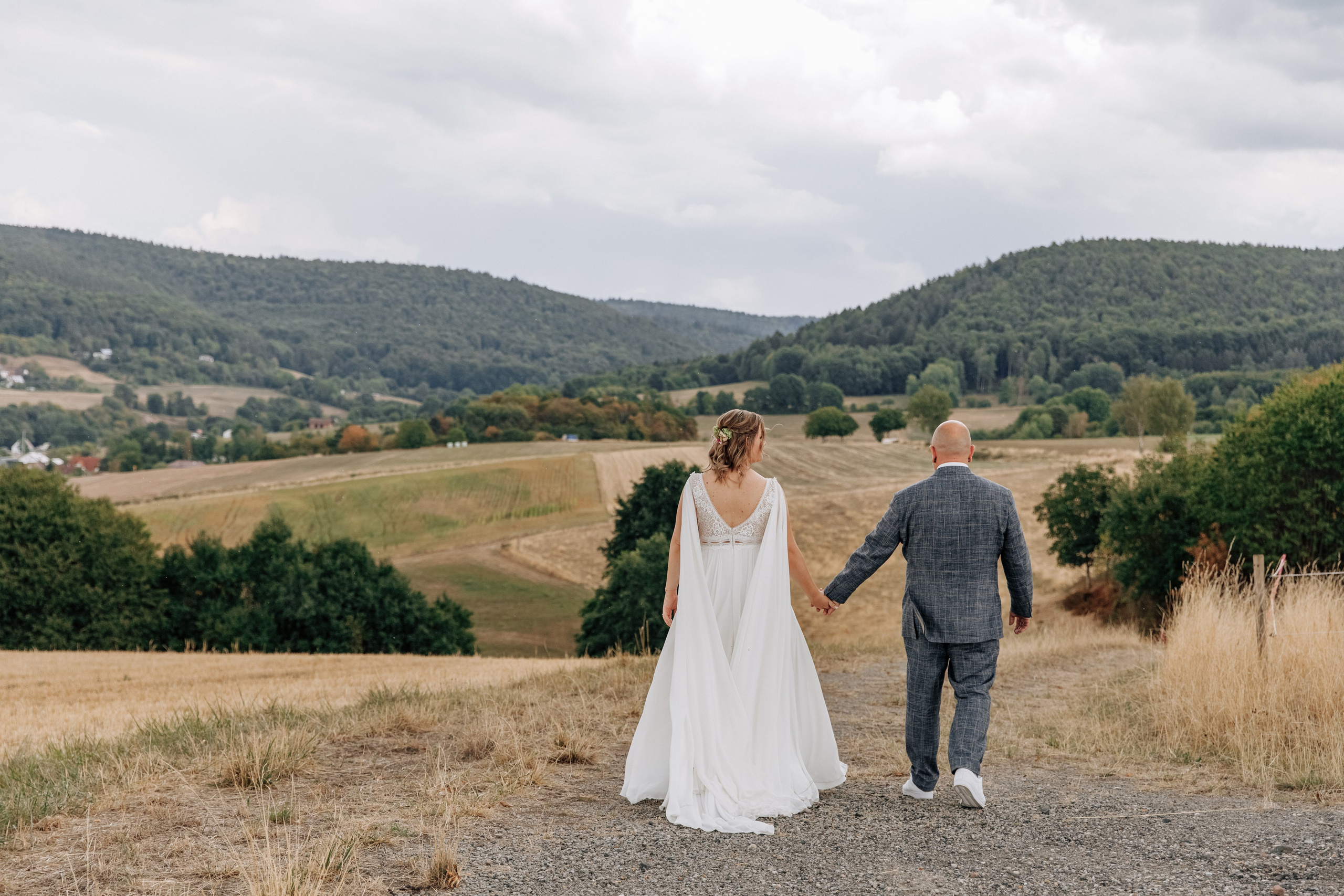Bräutigam und Braut spazieren vor der Weite der fränkischen Felder bei Aschaffenburg.